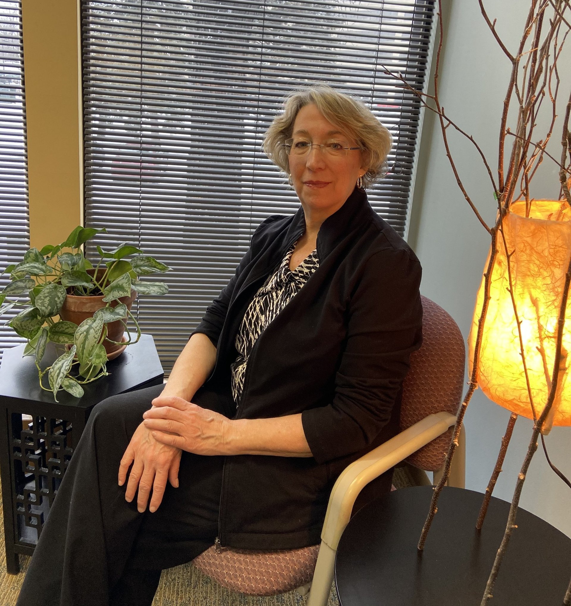 Dr. Jennifer Naas sitting in front of a window with closed blinds, creating a calm and focused setting.