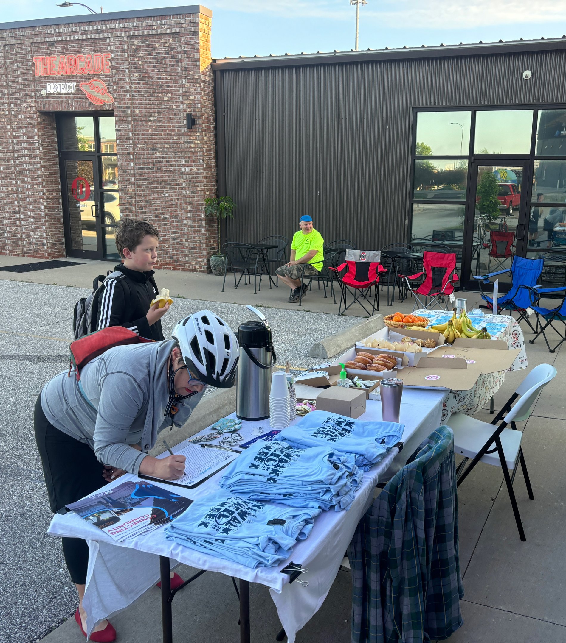 Mayor Barbara Buffaloe, wearing a bike helmet, filling out her name, at a table with pastries