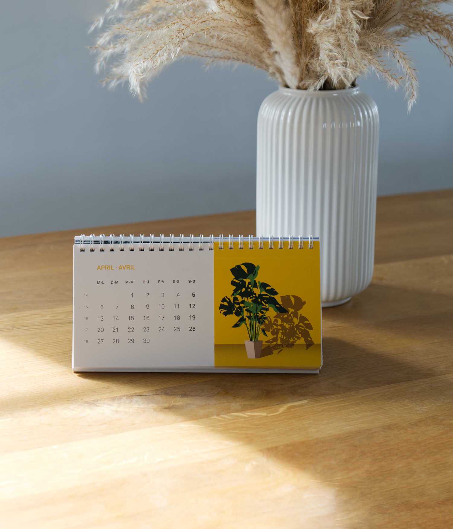 Tischkalender für April auf einem Holztisch, mit einer weissen Vase im Hintergrund.