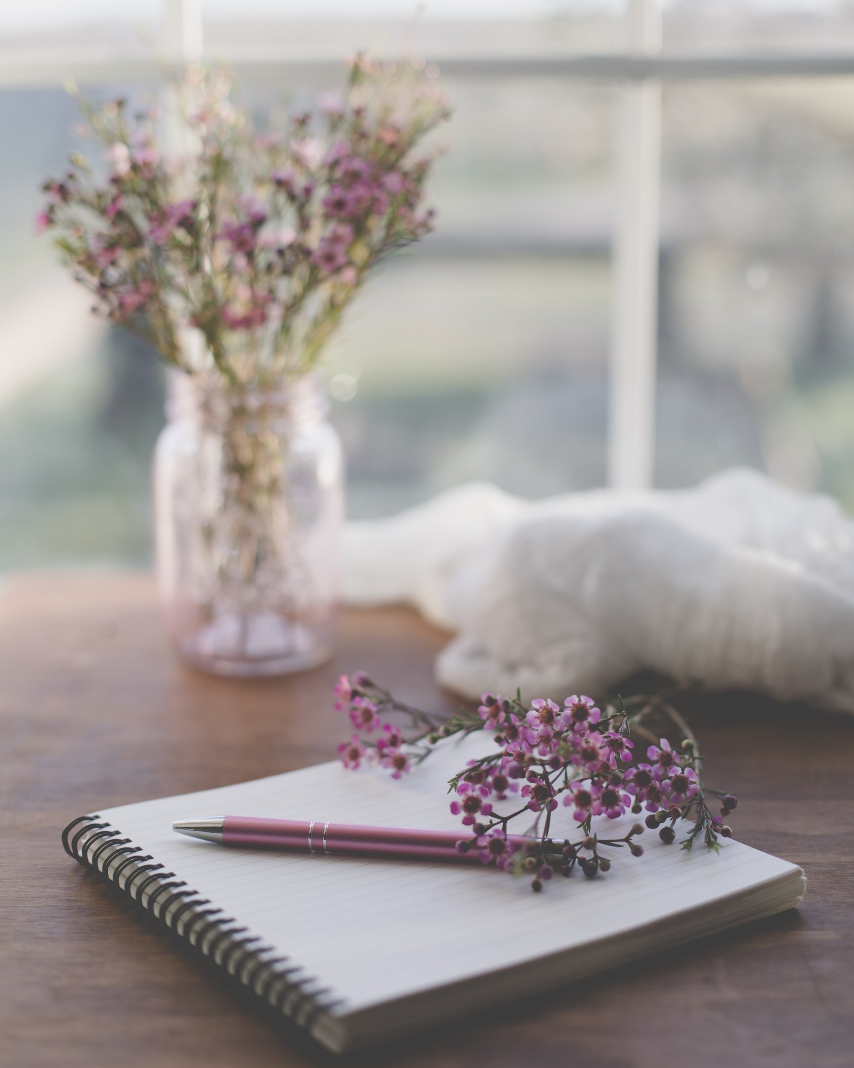 pink pen on spiral notepad with pink flowers nearby