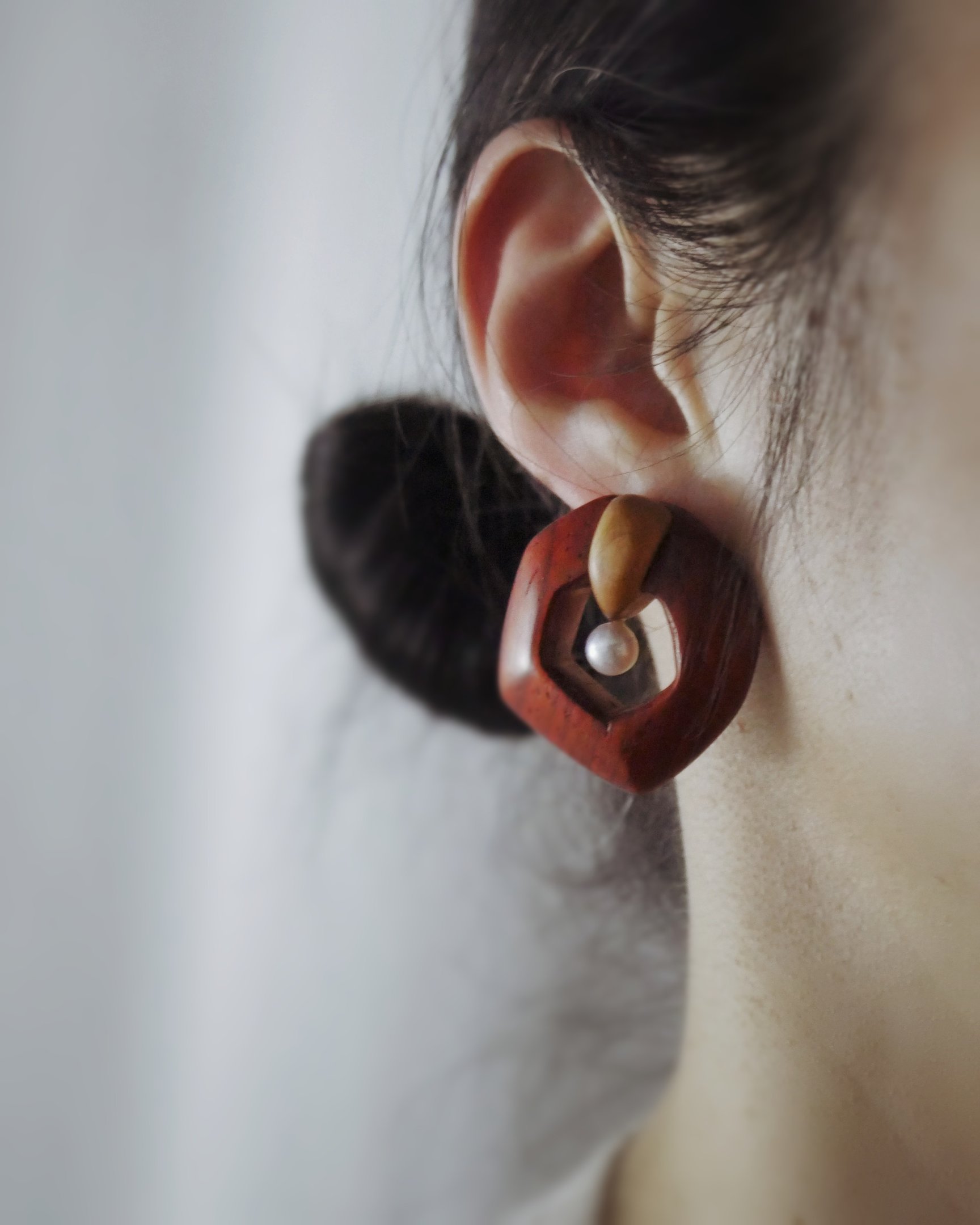 Handmade wooden geometric earring with a white pearl accent worn on a person's ear.