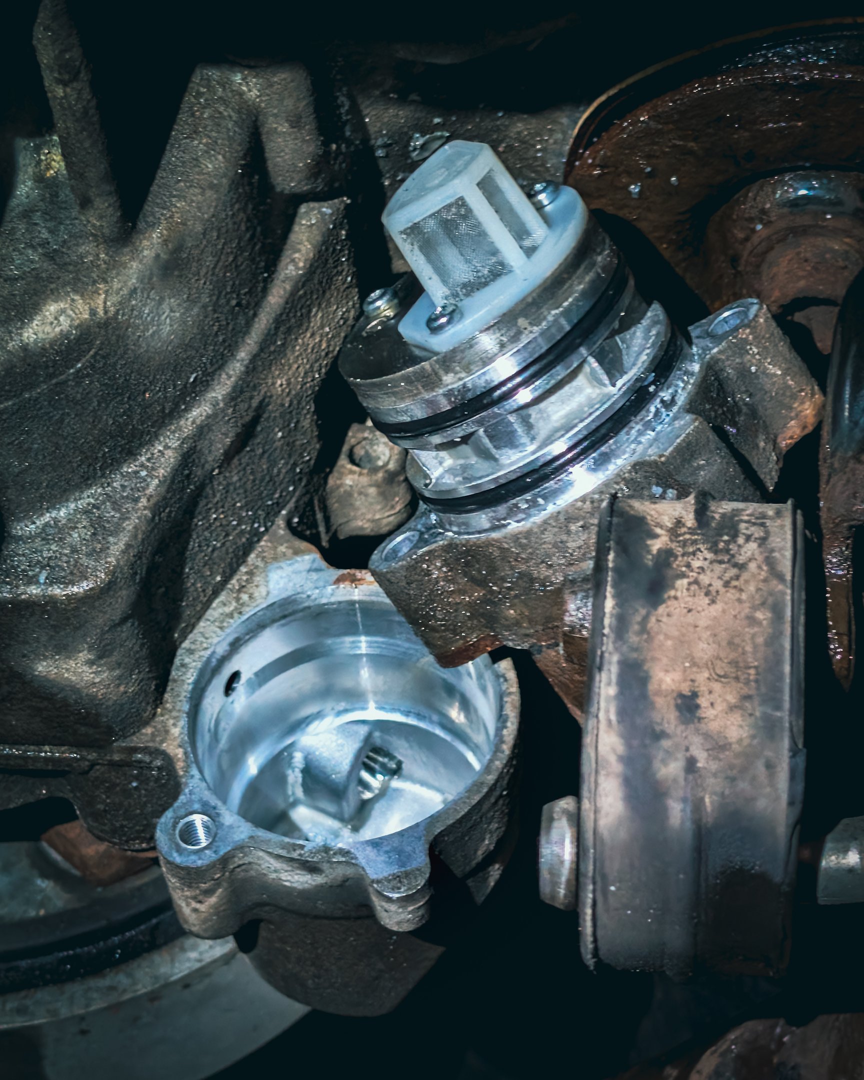 Close-up of a clean car oil pump screen and filter assembly being installed into a greasy engine housing.