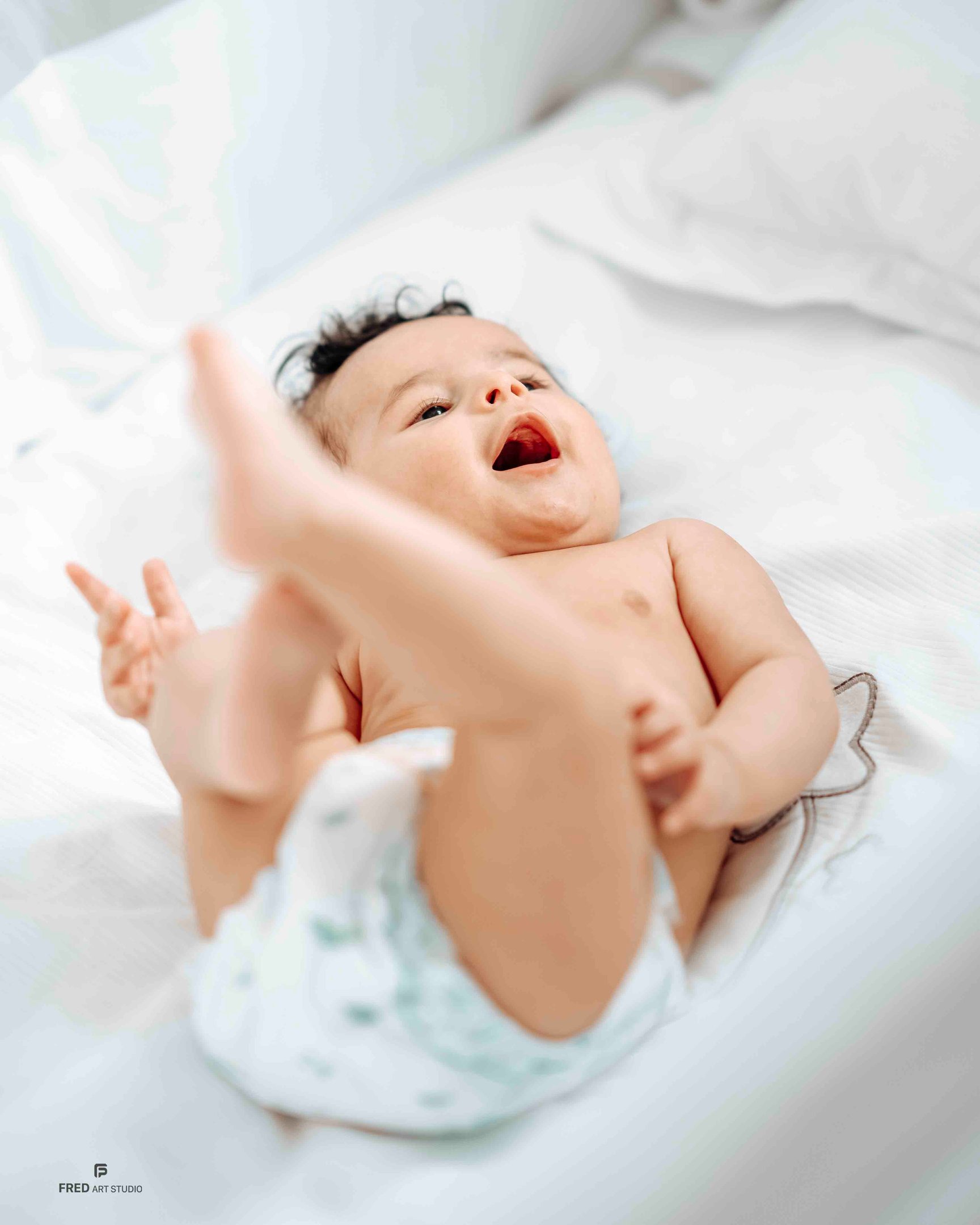 Smiling baby lying on bed – natural newborn photography by Fred Art Studio London