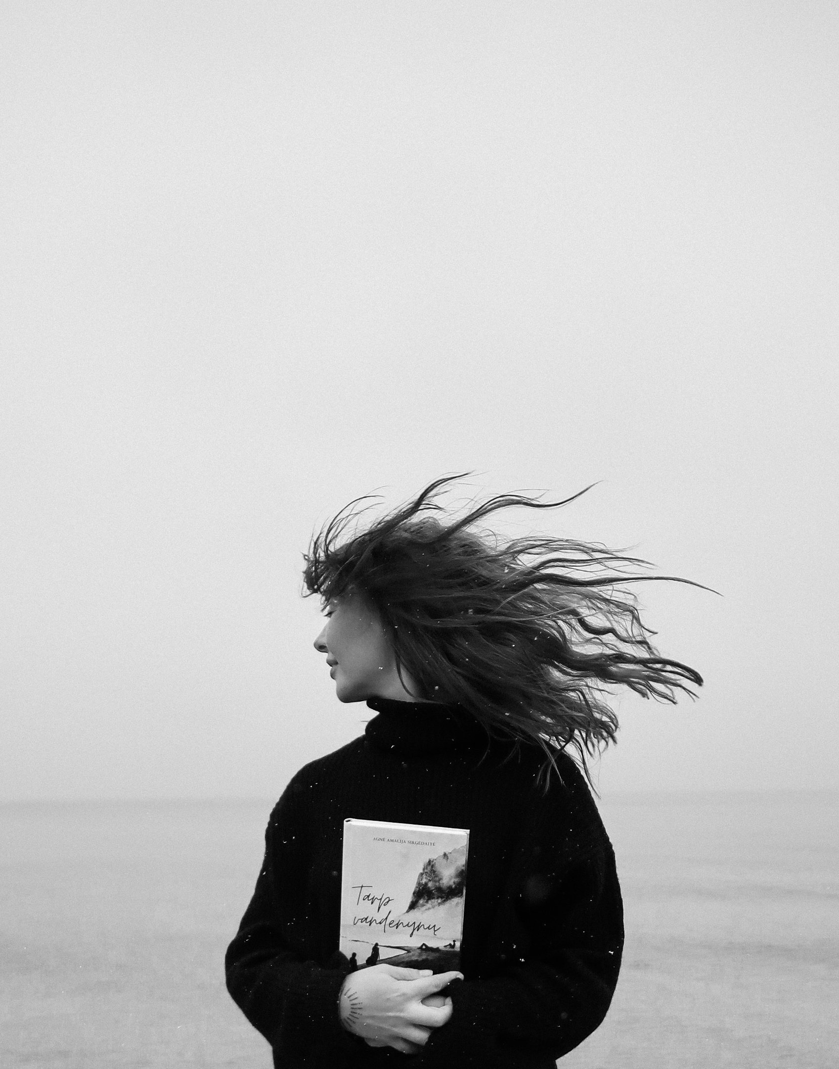 a woman standing on a beach holding a book