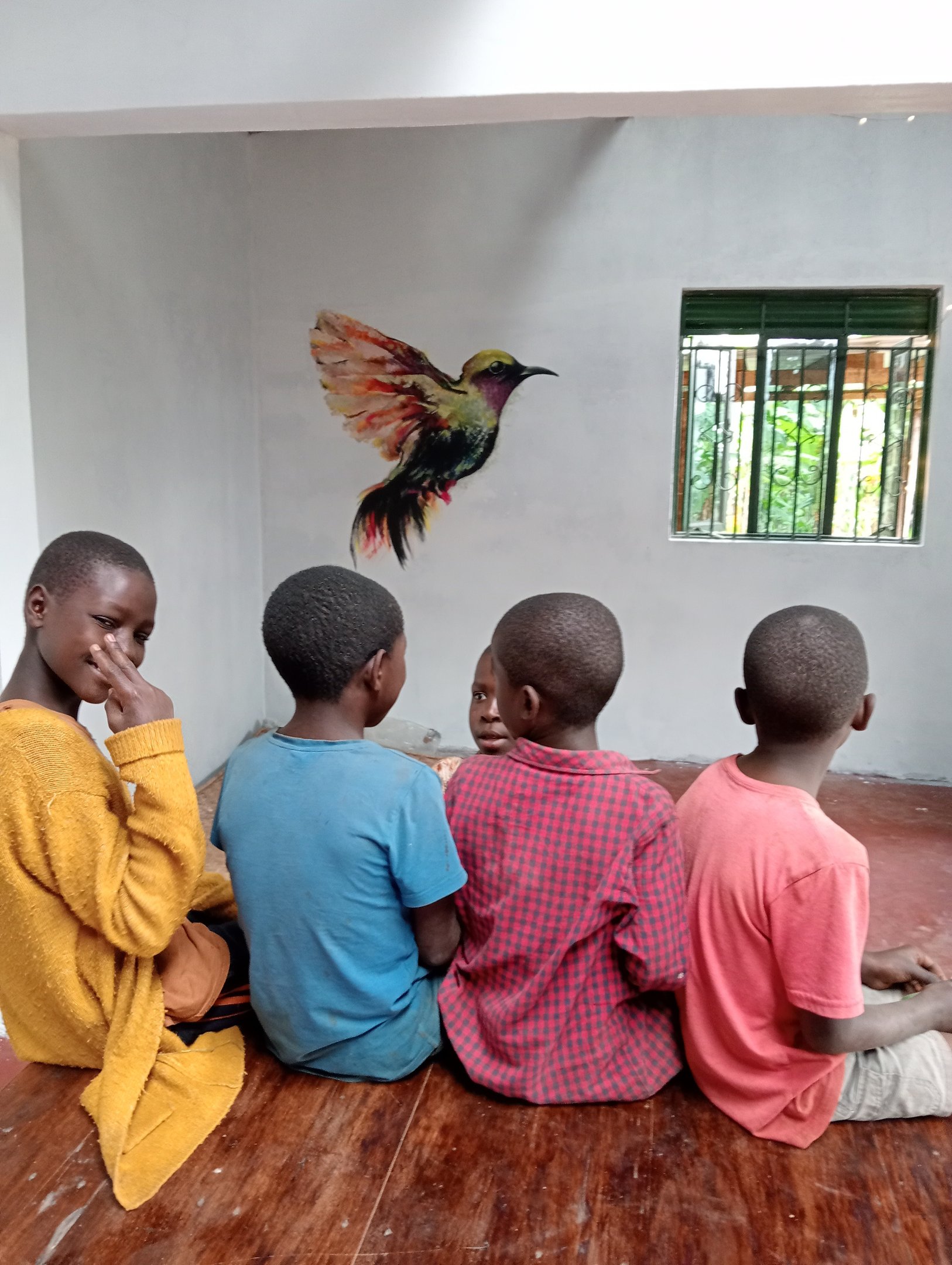 Image of 4 children in front of bird mural, with one looking back at the camera.