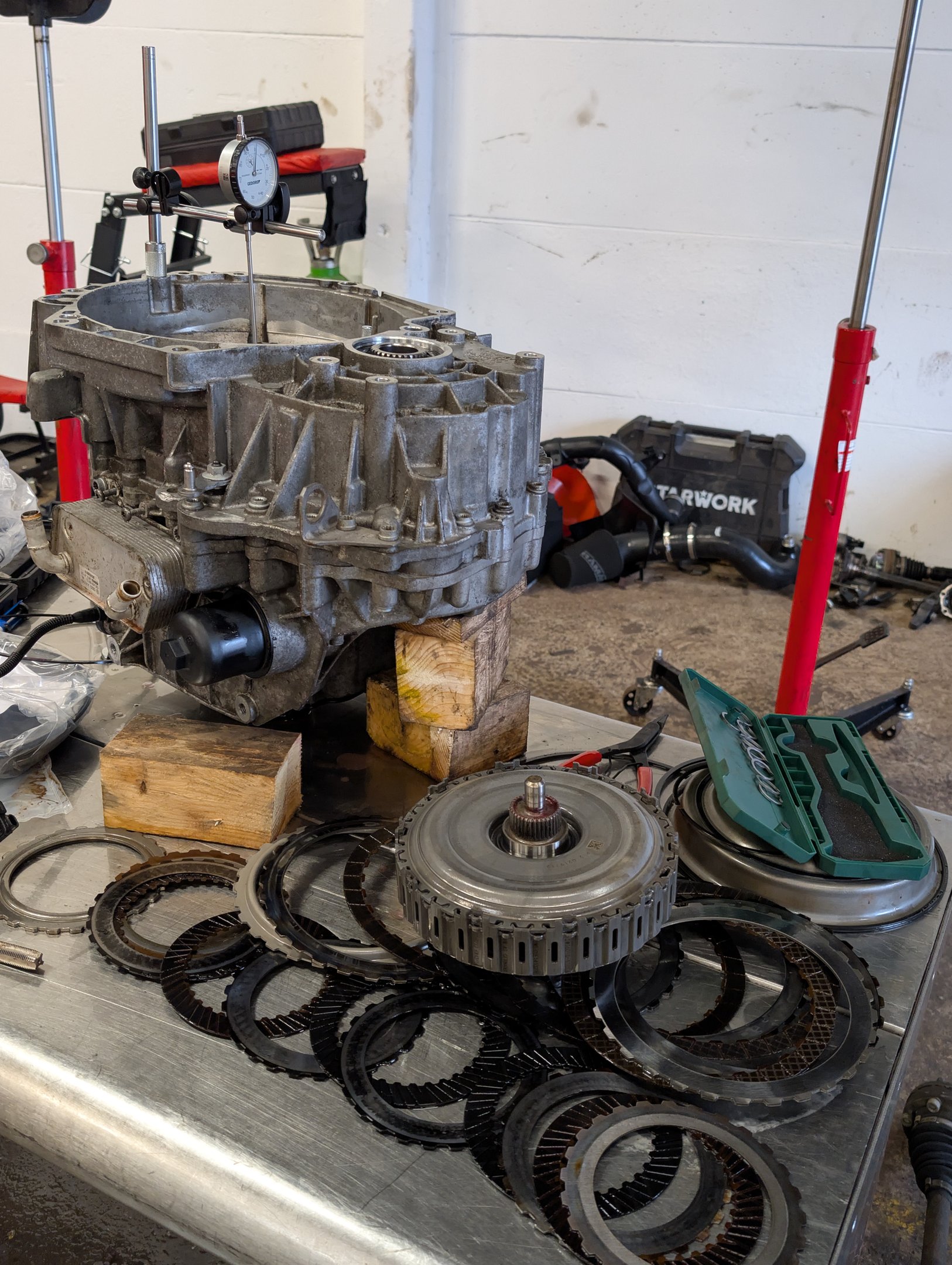 Automatic transmission rebuild with clutch plates and dial indicator tool on a metal workbench.