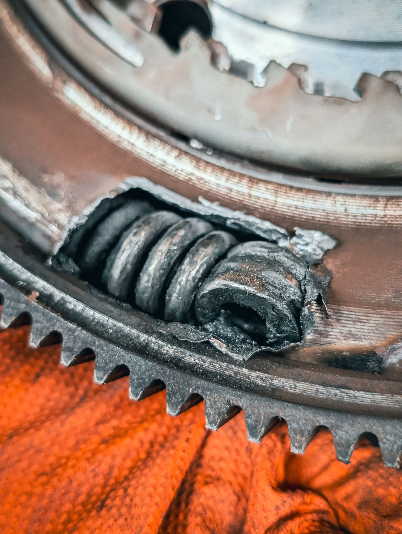 Close-up of a damaged dual mass flywheel with a broken internal damper spring and cracked metal housing.