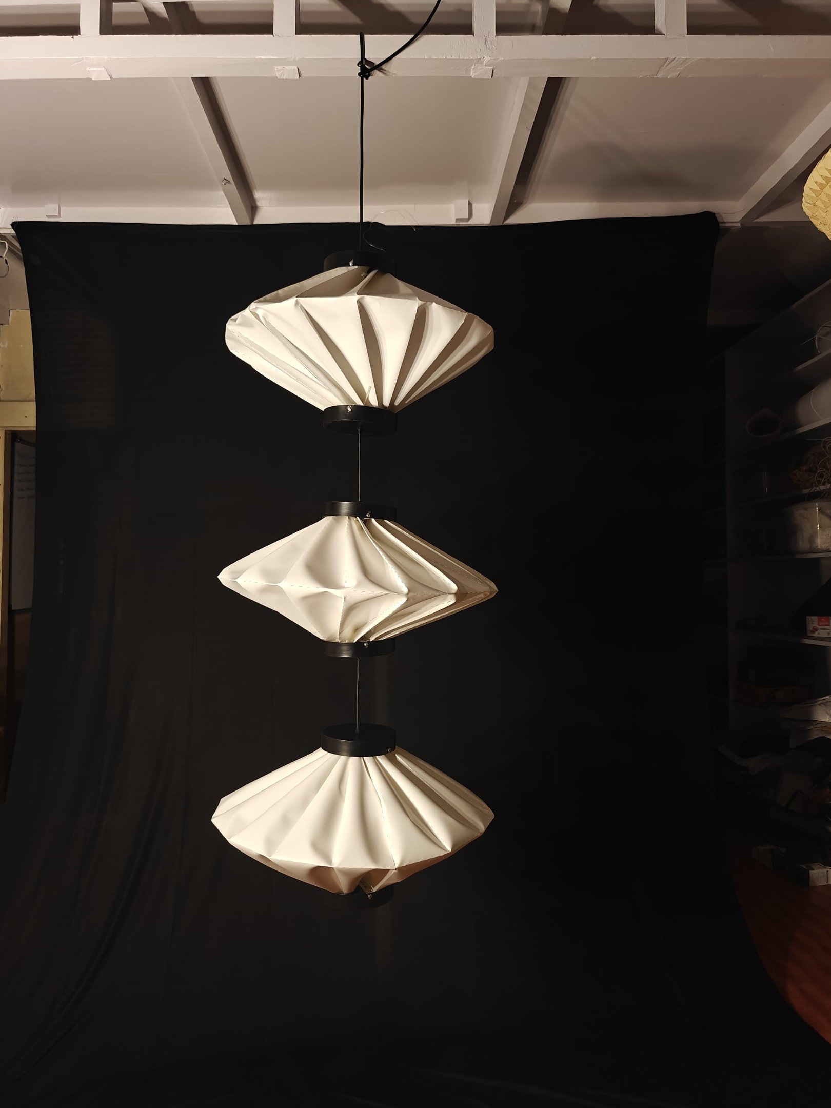 Dumpling shaped modern pleated paper light hanging against a black backdrop.