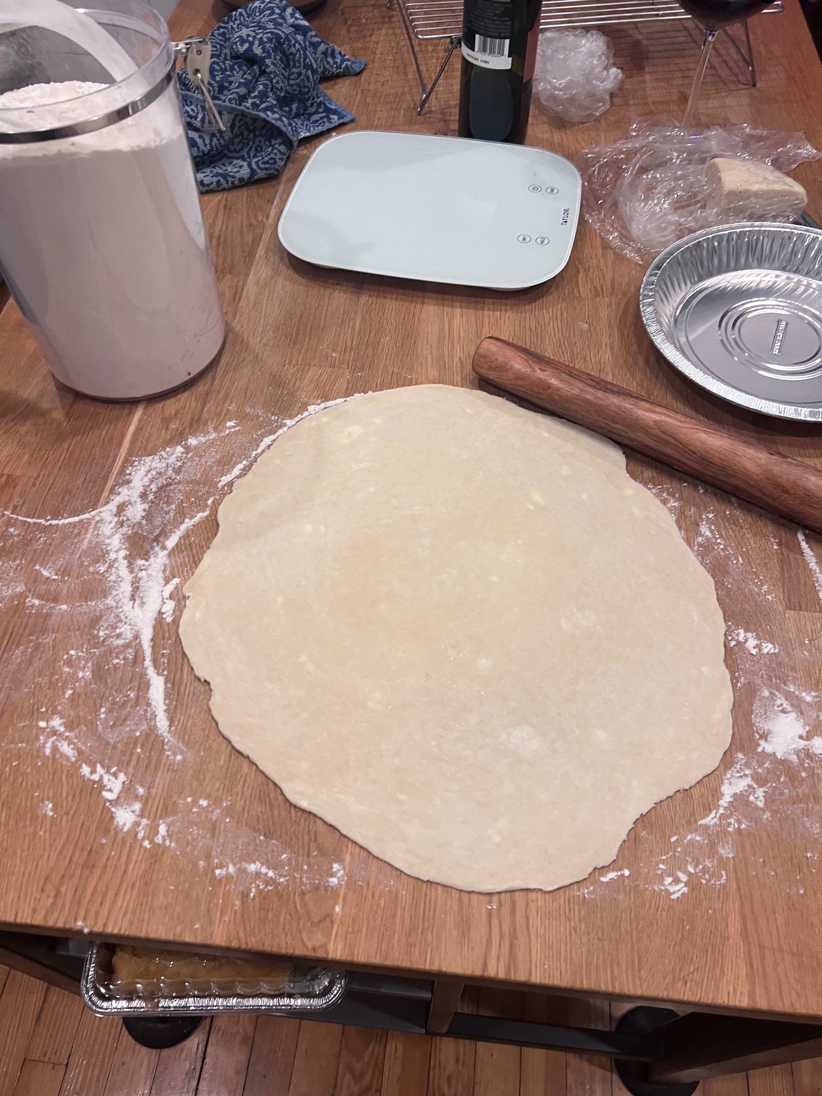 Rolled out pie crust dough on a floured wooden table with a rolling pin and baking supplies.