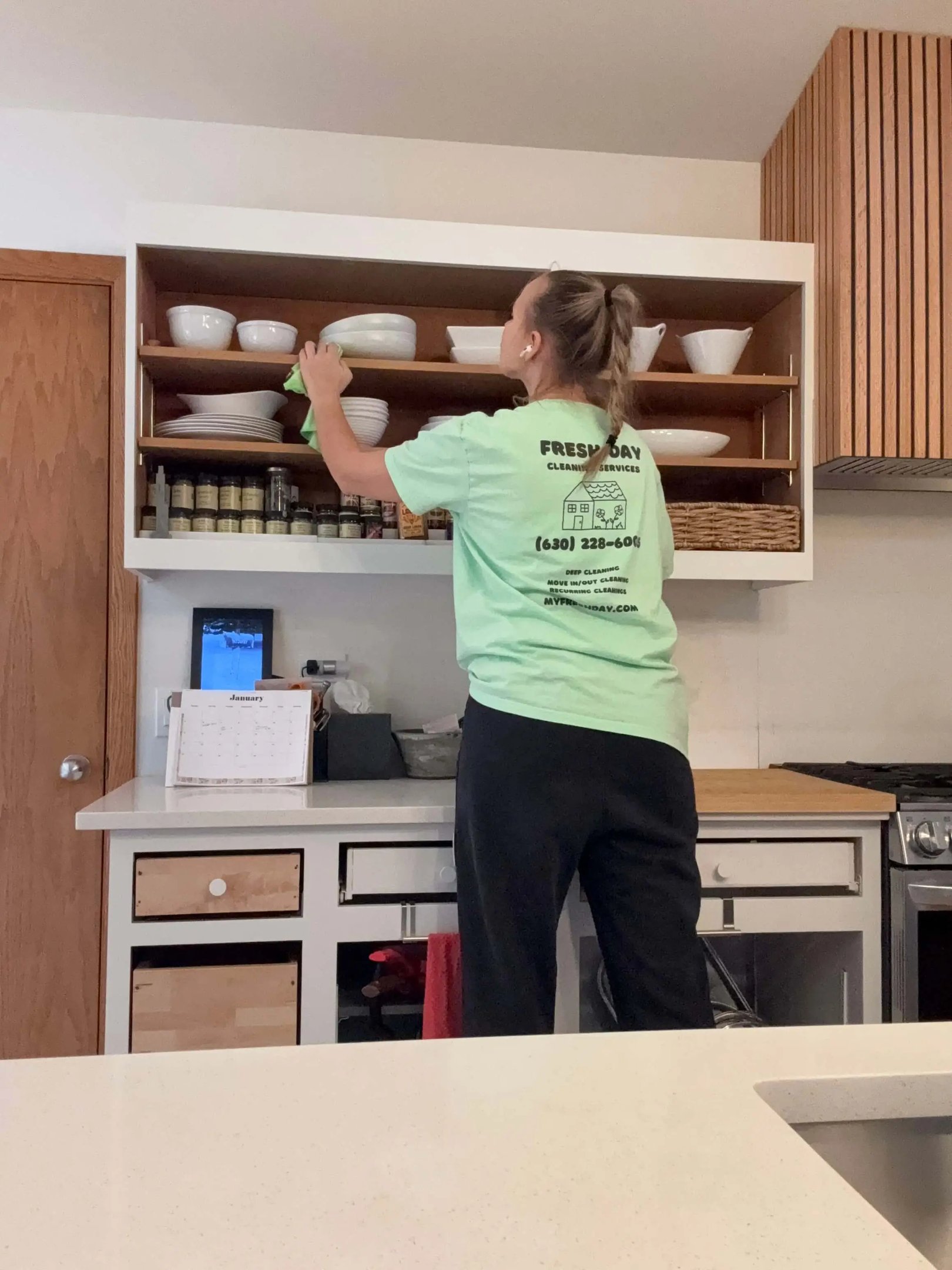 A professional cleaner thoroughly cleans a kitchen shelf with dishes