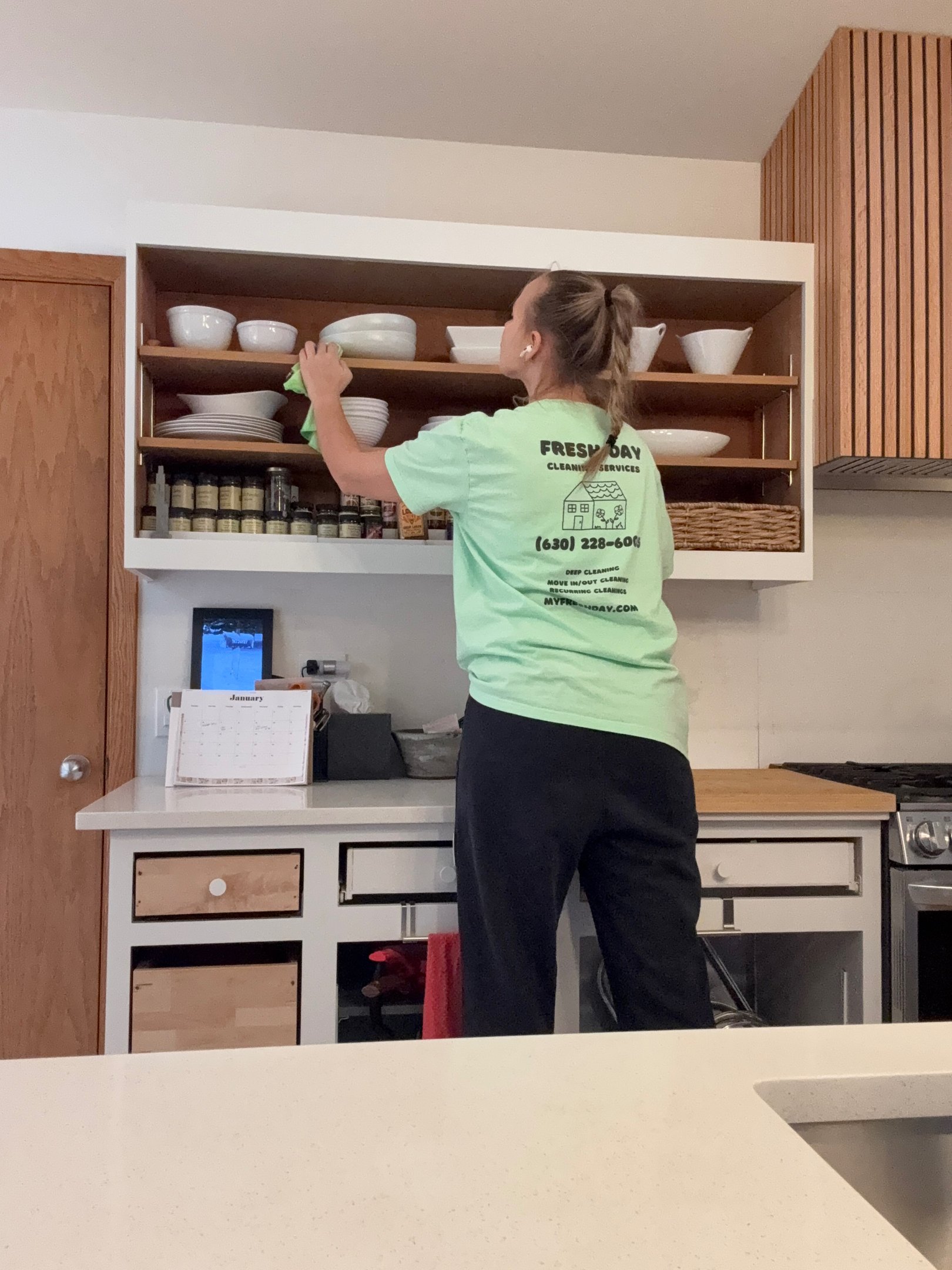 A professional cleaner thoroughly cleans a kitchen shelf with dishes