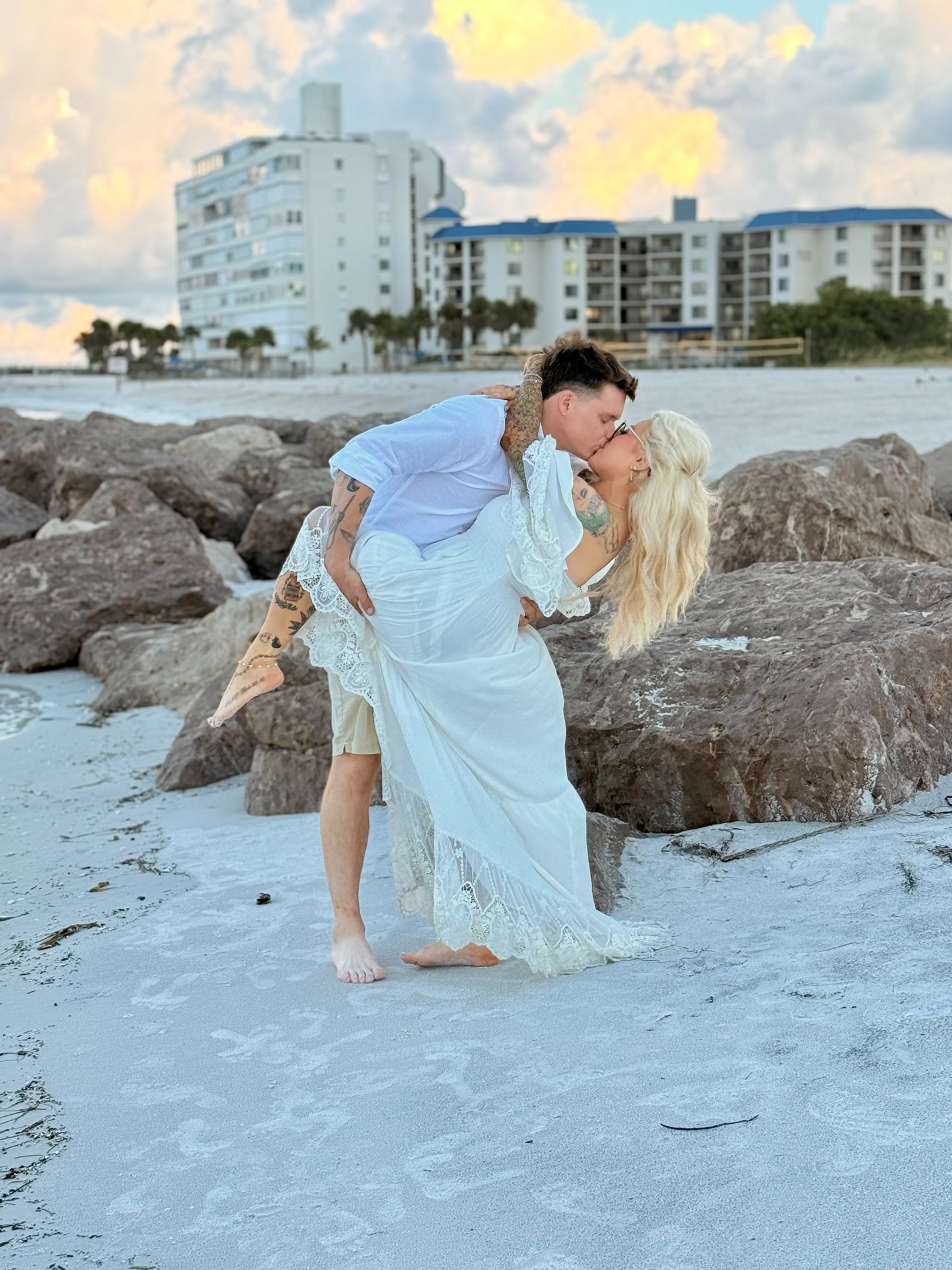 Couple kissing on a tropical beach at sunrise during a romantic wedding photoshoot by the ocean.