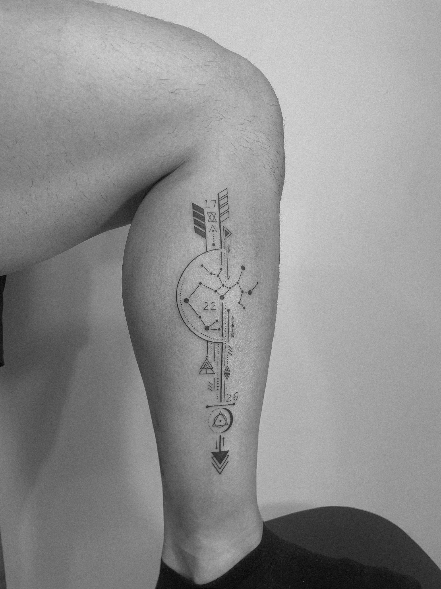 Tatuaje geométrico flecha con constelación y símbolos en pierna madrid