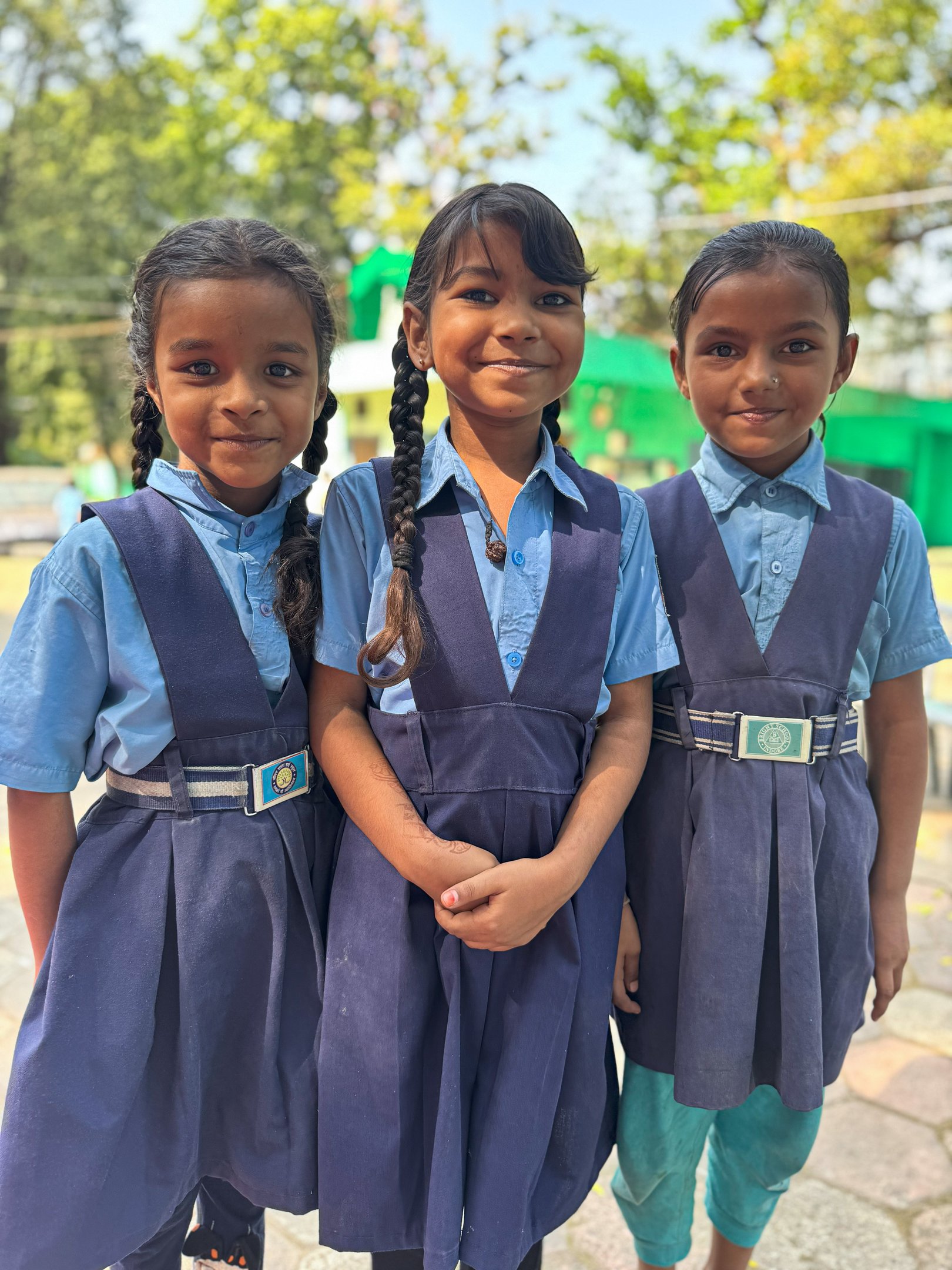 Three young schoolgirls in blue uniforms standing together smiling outdoors