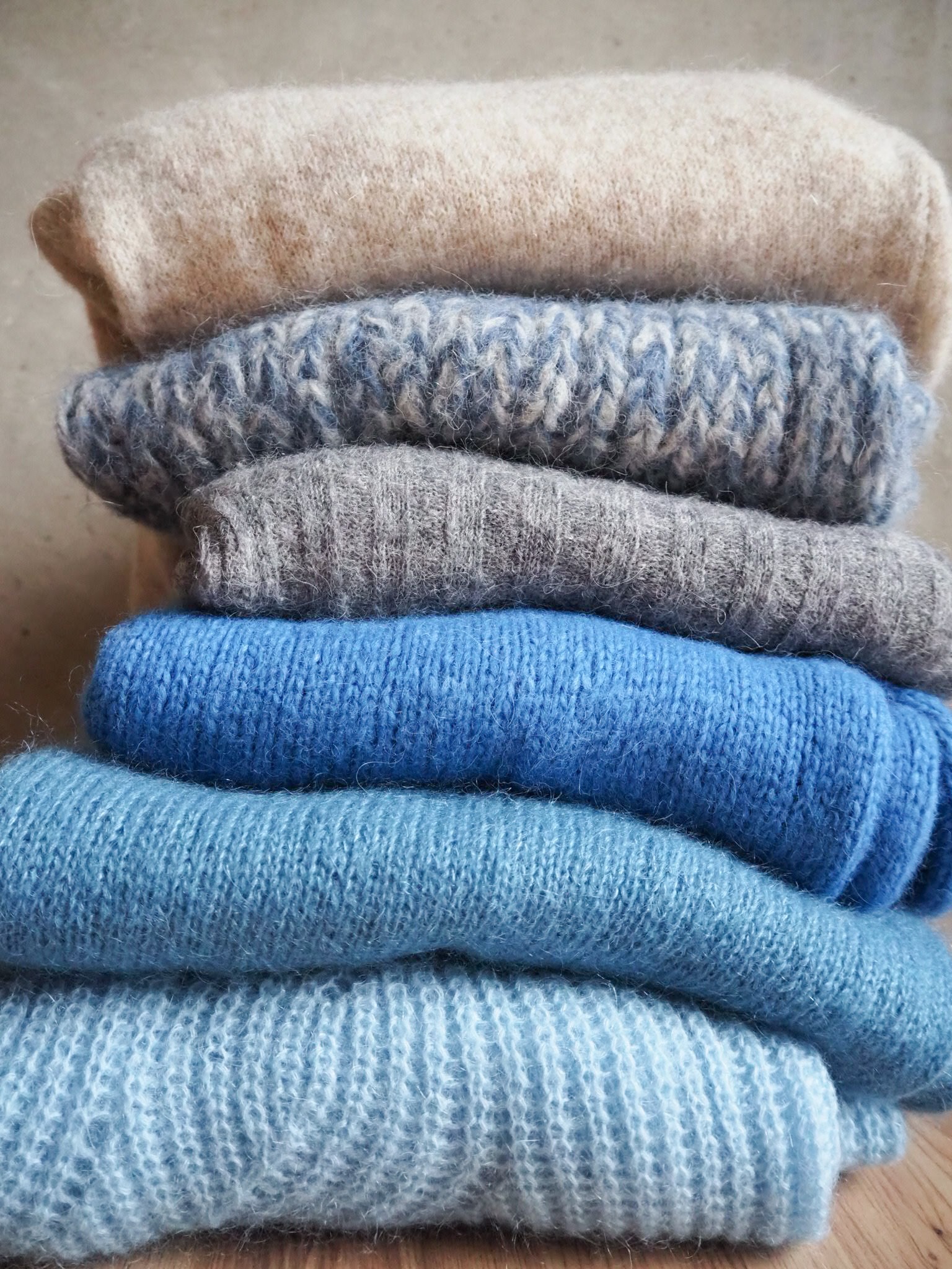 szare i niebieskie swetry ułożone w stos na tle szarej ściany