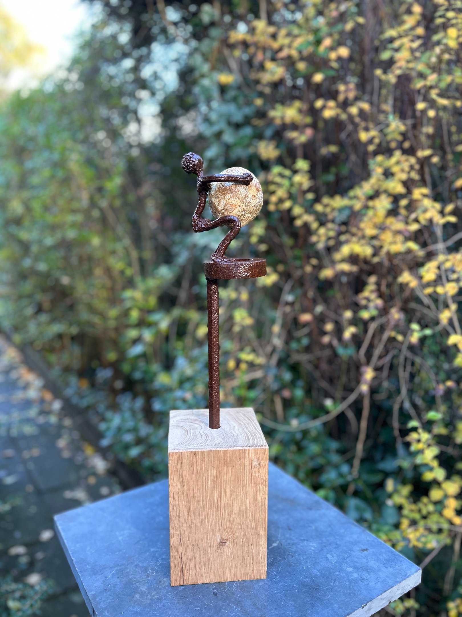 Iron sculpture with stone on wooden pedestal