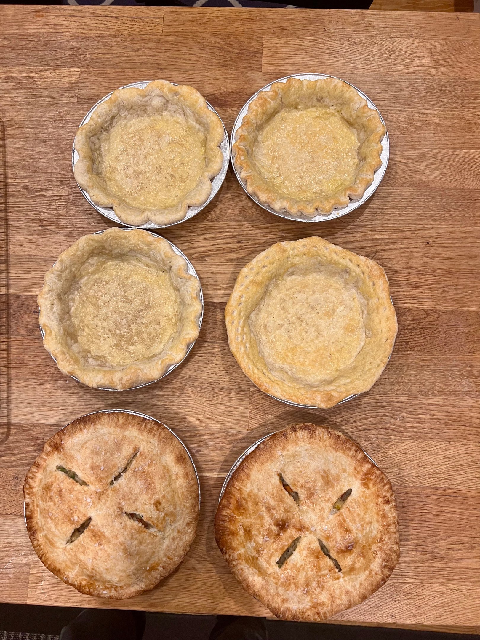 Freshly baked golden brown pie crusts and fruit pies cooling on a wooden table.