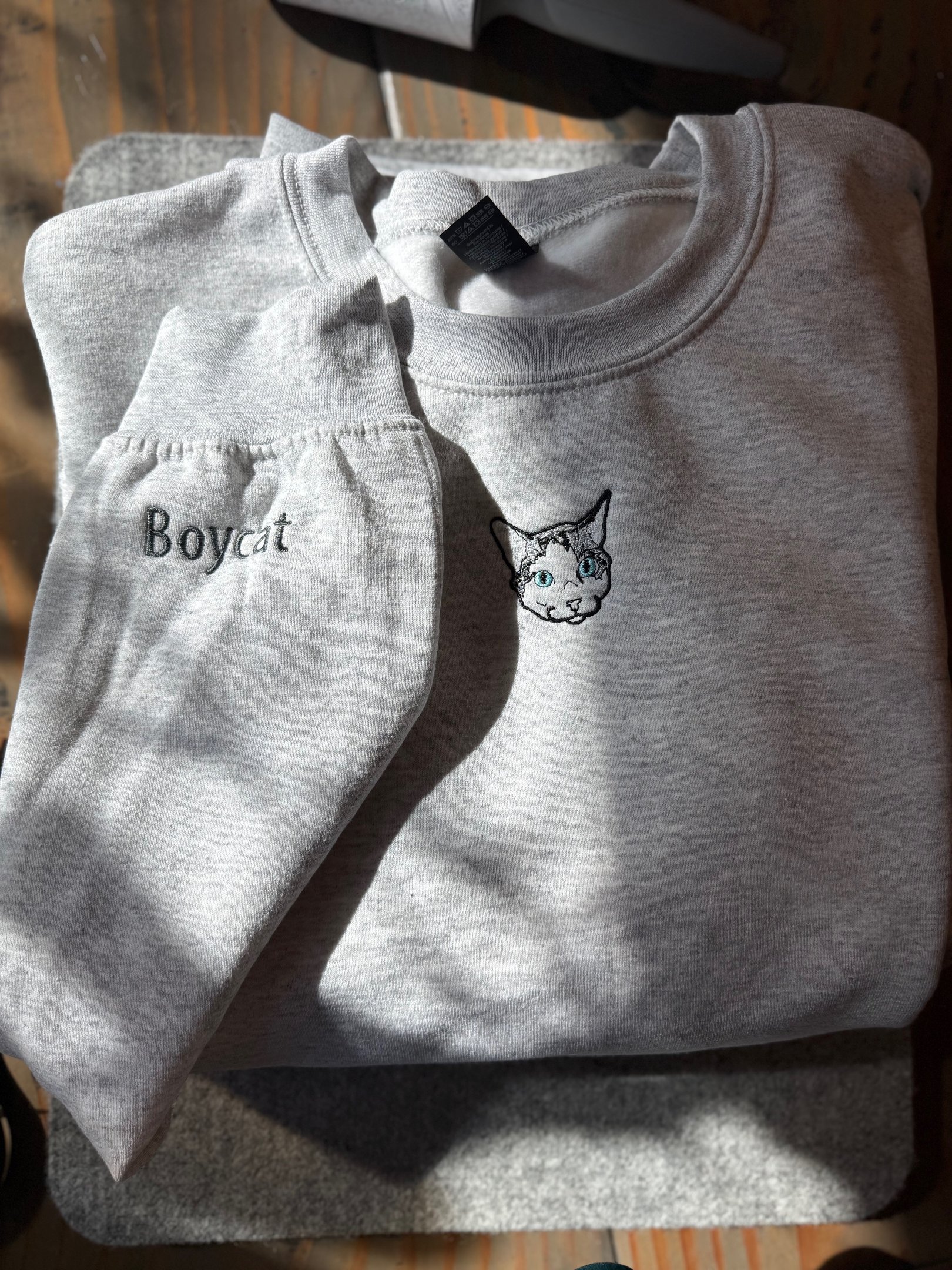 a light gray sweatshirt with a picture of a cat embroidered on it