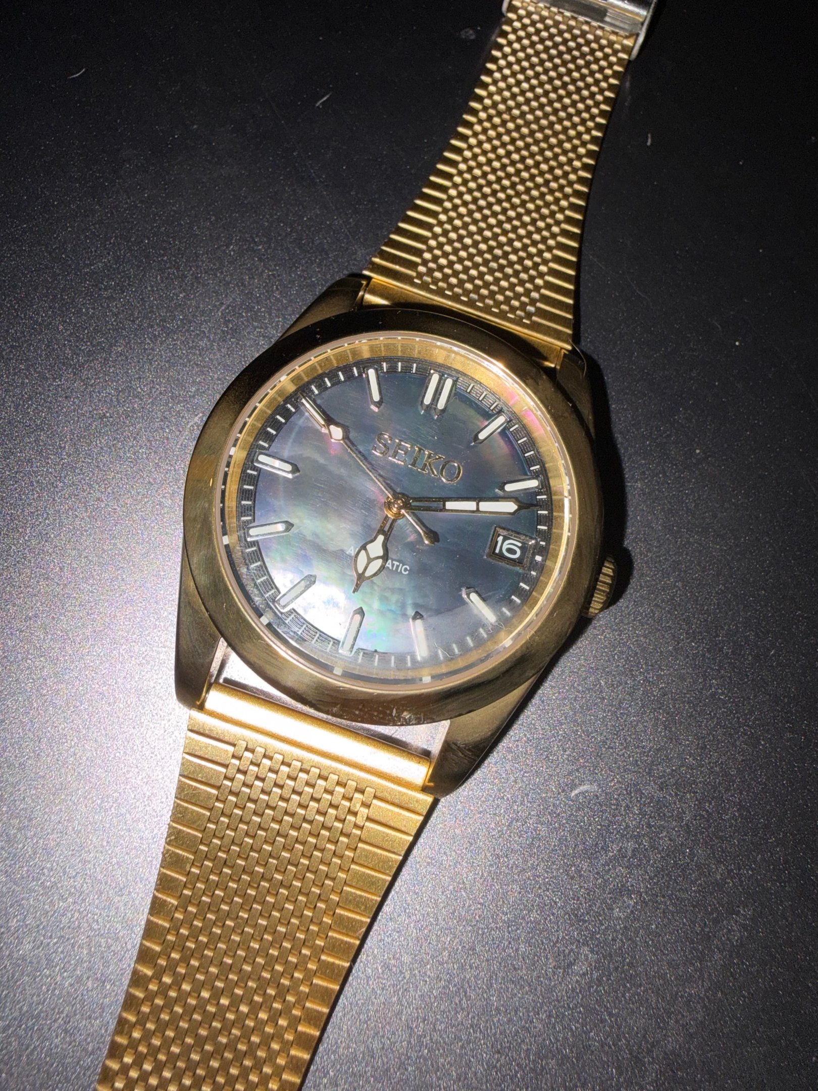 Gold Seiko automatic watch with a black mother of pearl dial and mesh bracelet strap.