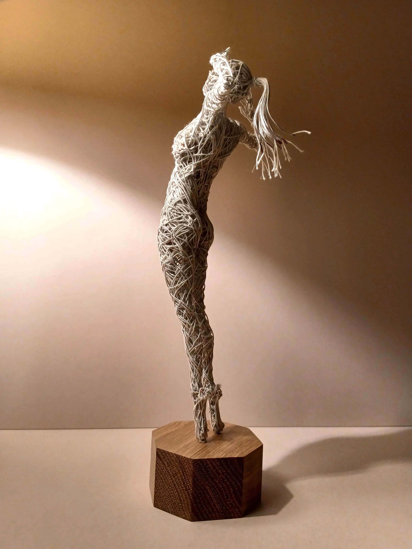 A cotton-covered wire sculpture of a standing female figure stretching with arms raised