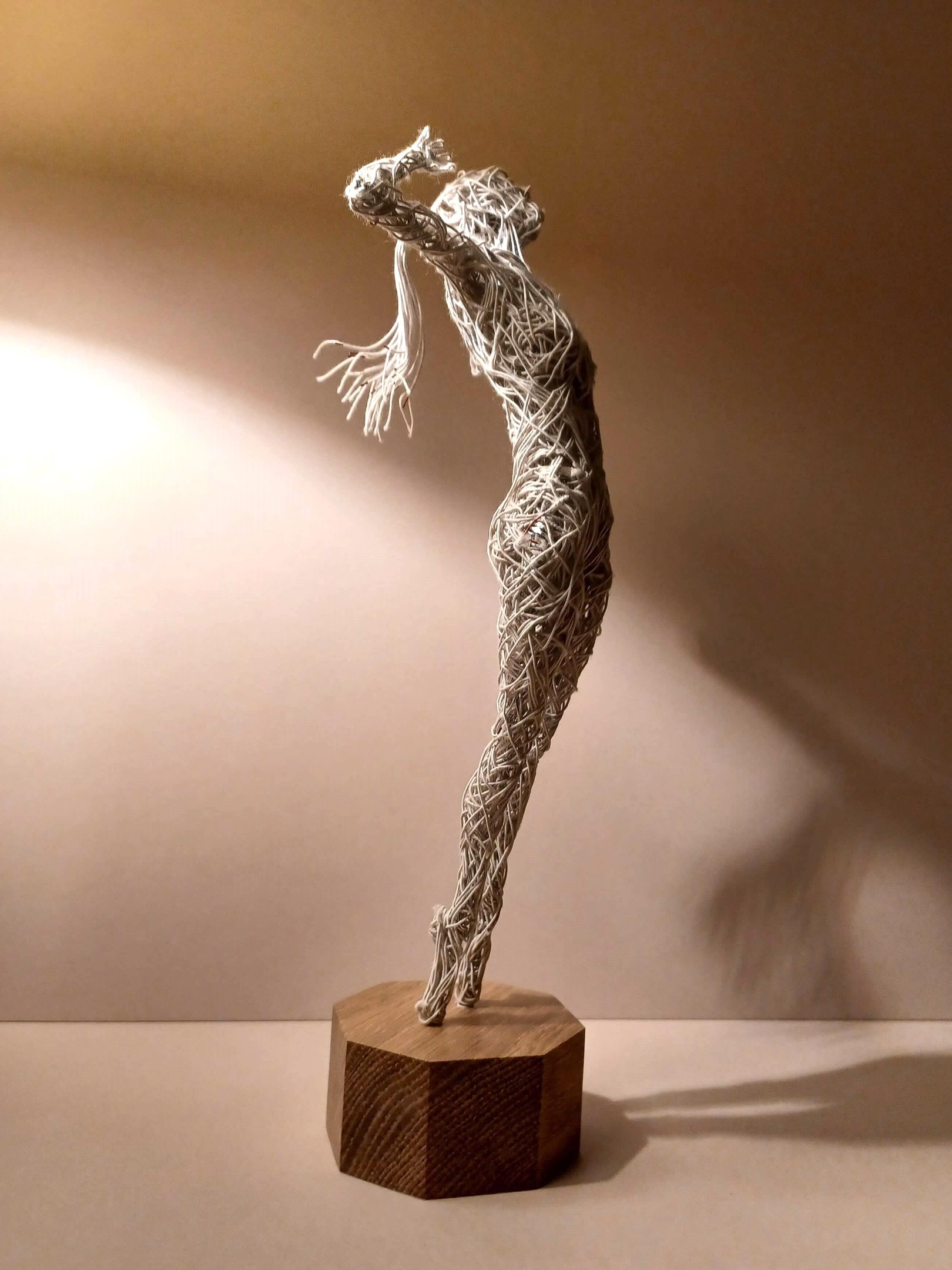 A cotton-covered wire sculpture of a standing female figure stretching with arms raised