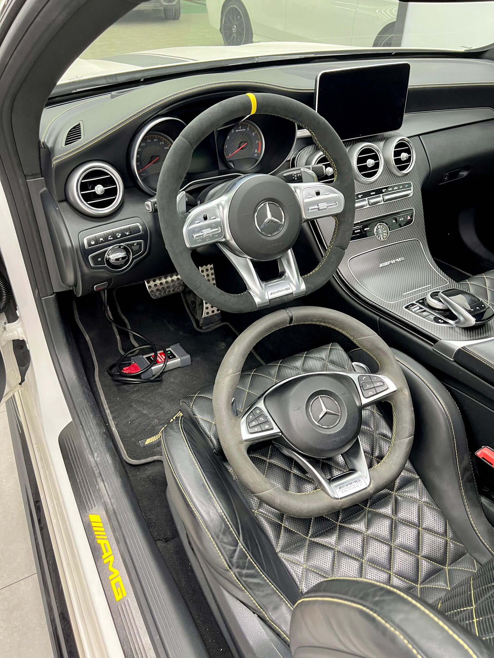 Interior of a Mercedes-Benz AMG featuring Alcantara steering wheels and yellow-stitched leather bucket seats.