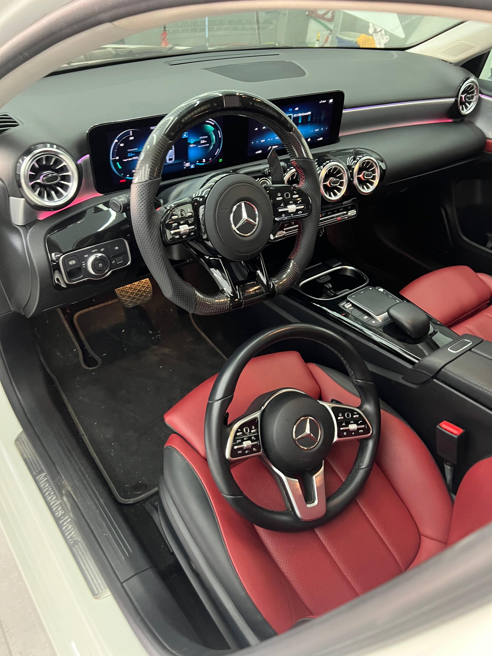 Luxury Mercedes-Benz interior featuring a carbon fiber steering wheel upgrade and red leather seats.
