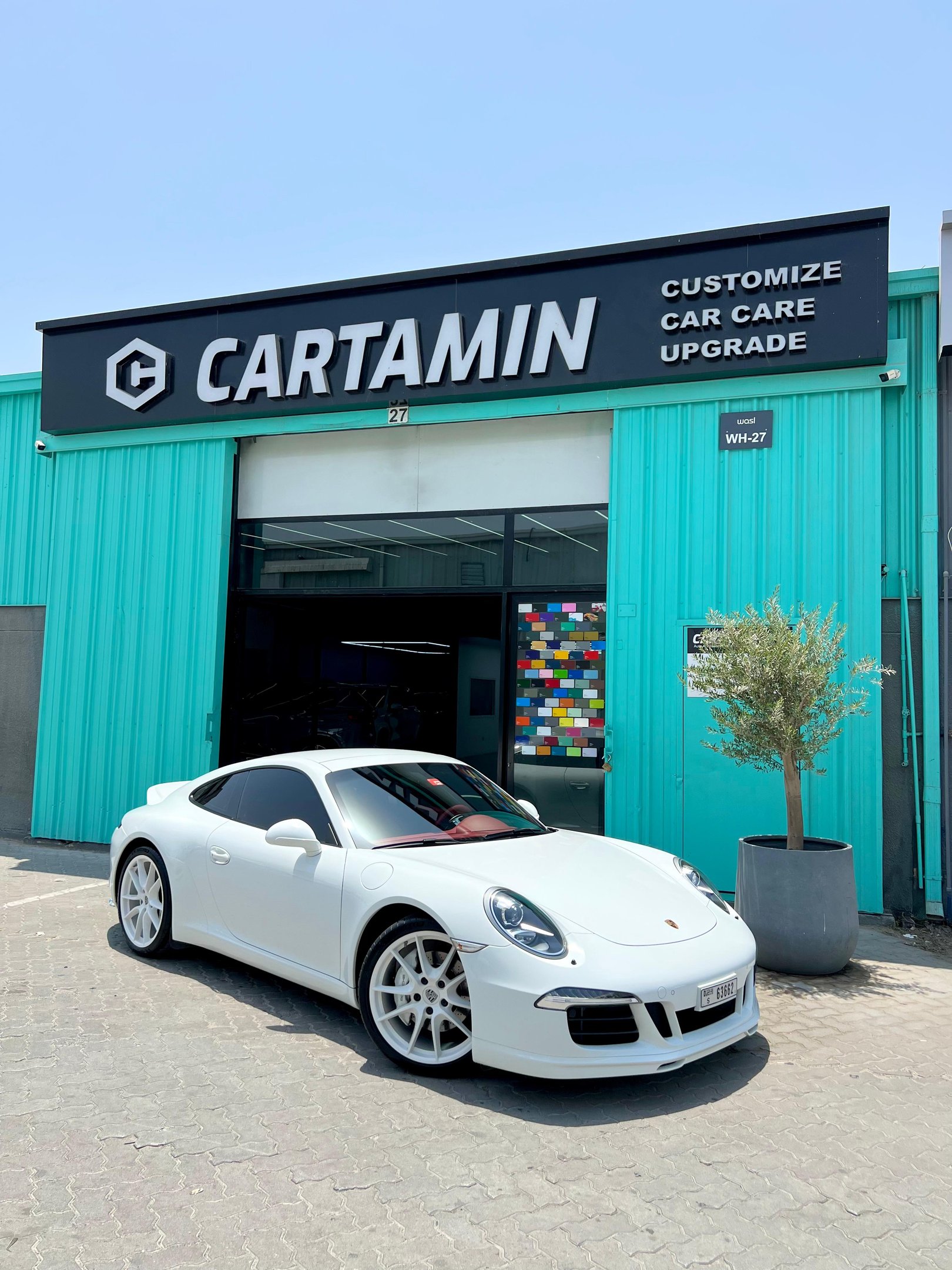 White Porsche sports car parked outside Cartamin car care and customization shop.