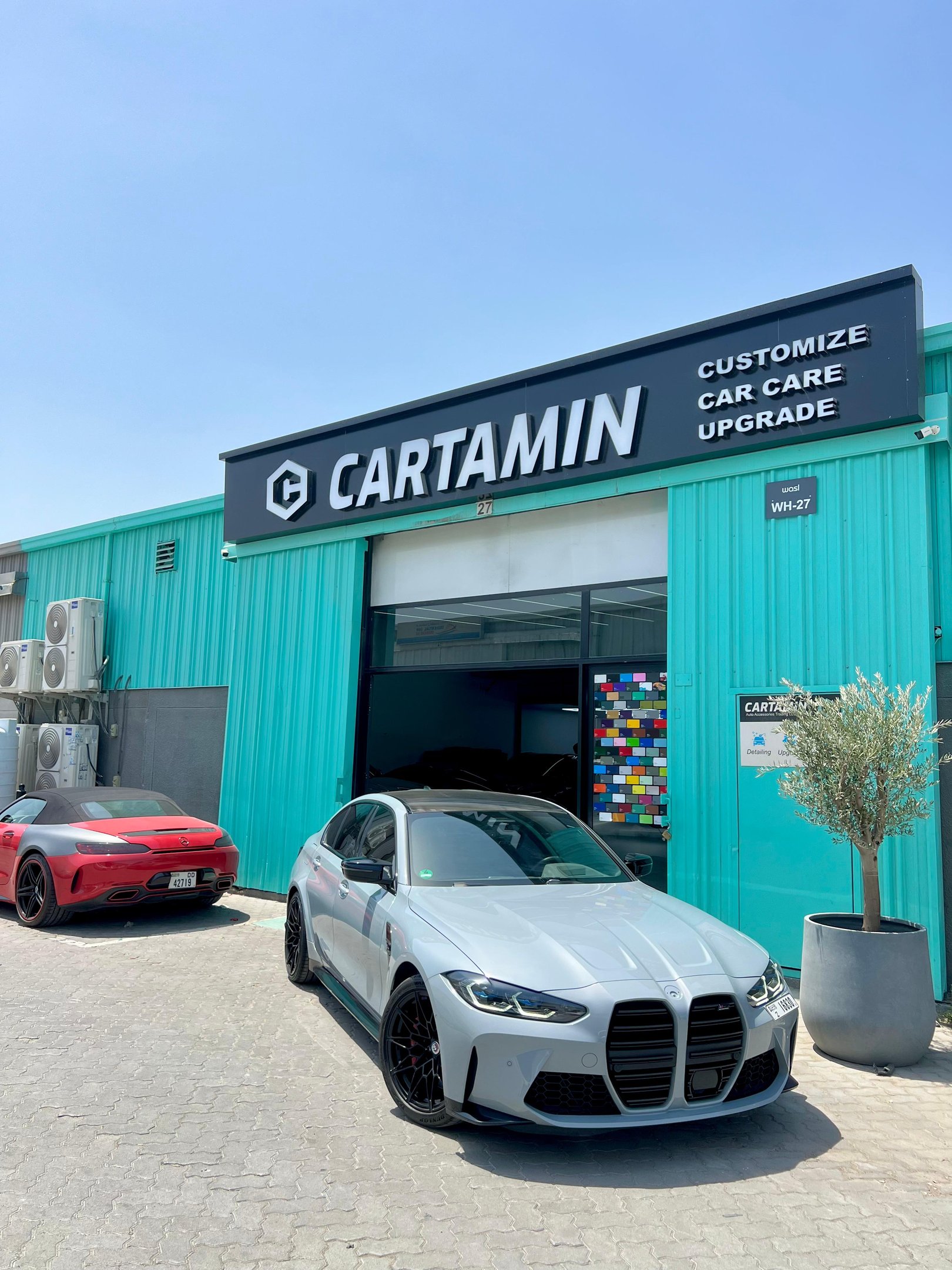 A grey BMW M3 parked outside the Cartamin car care and customization shop in Dubai.