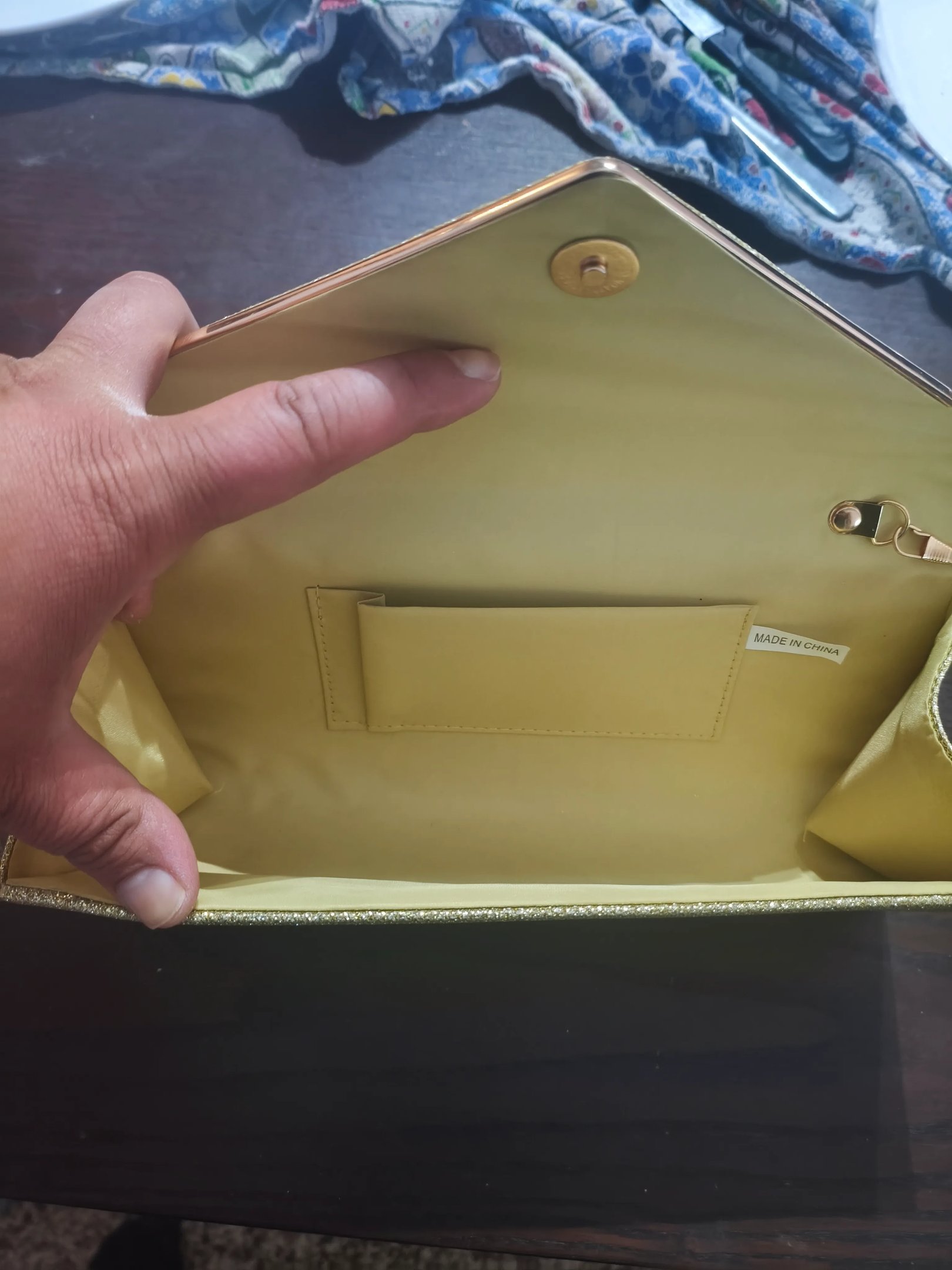 Análise do espaço interior da mala clutch de festa com detalhe do bolso interno para cartões.