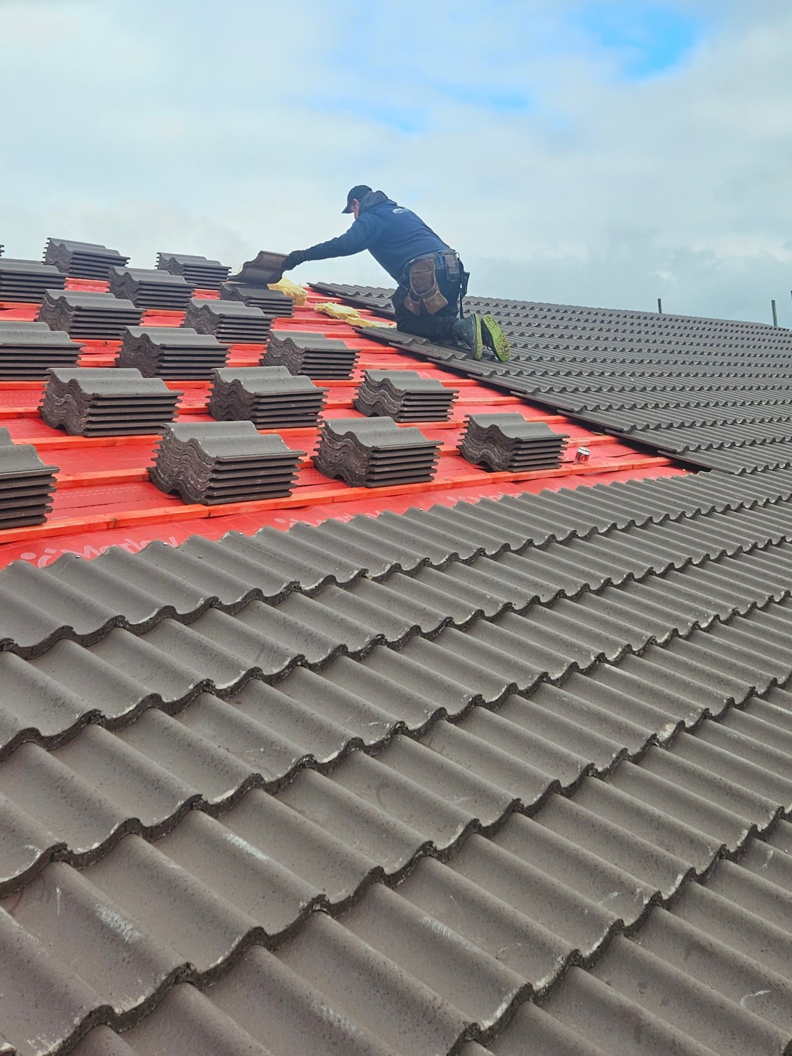 Professional roofer installing new concrete roof tiles on a residential house rooftop. in Essex