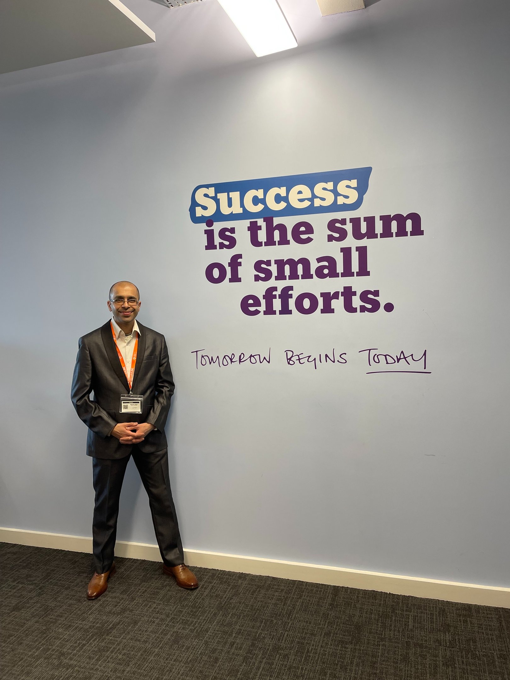 A businessman in a suit stands by an office wall with a motivational success quote.