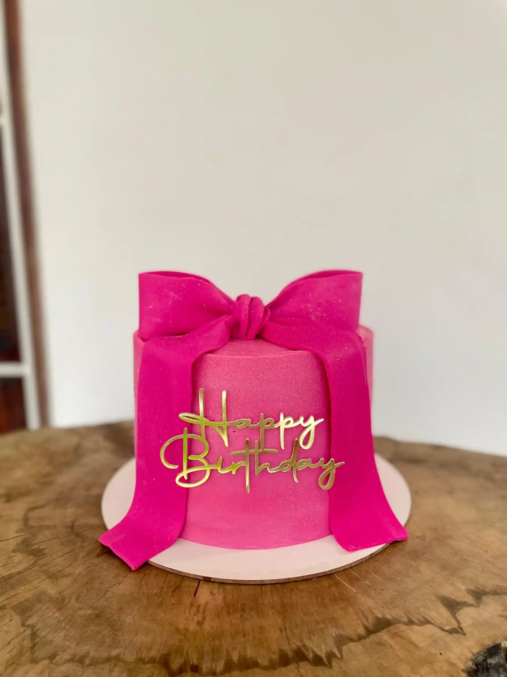 Bolo de aniversário decorado em rosa com fita e detalhes dourados. Ideal para festas e comemorações 