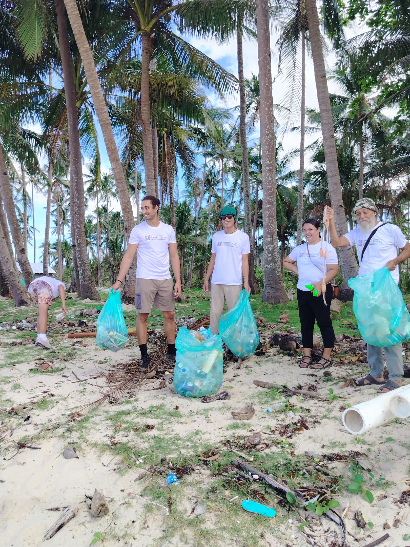 Volunteers cleaning up plastic waste in bags on a tropical beach with palm trees.