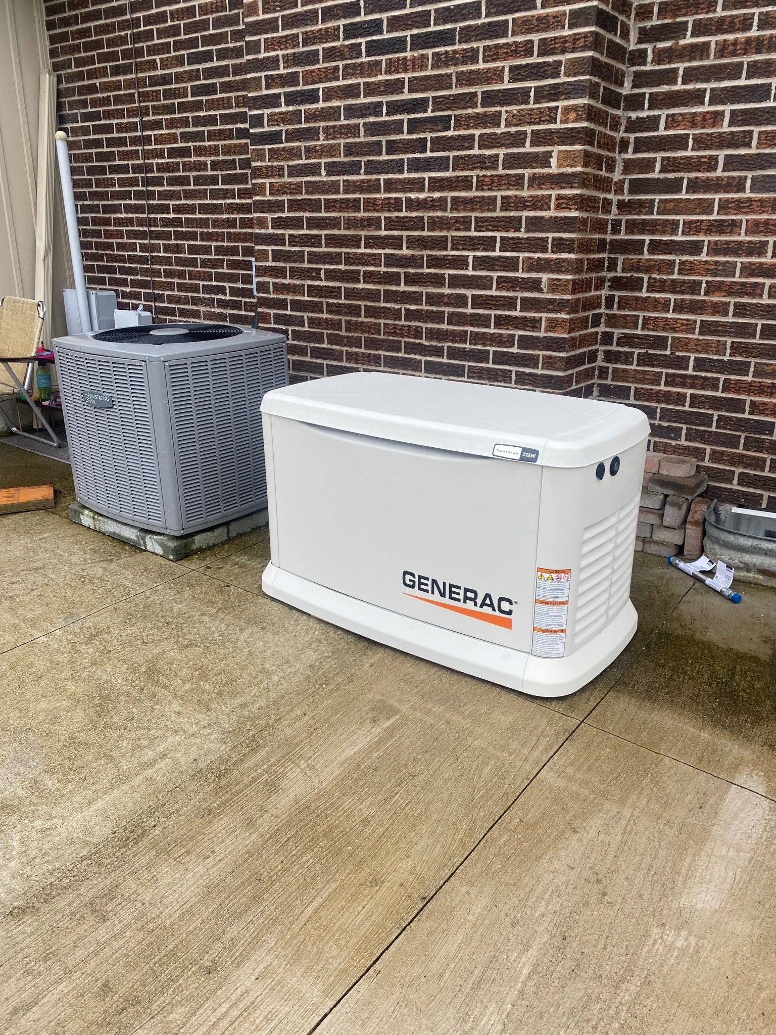 A white Generac home standby generator installed on a concrete pad next to an HVAC unit and brick wall.