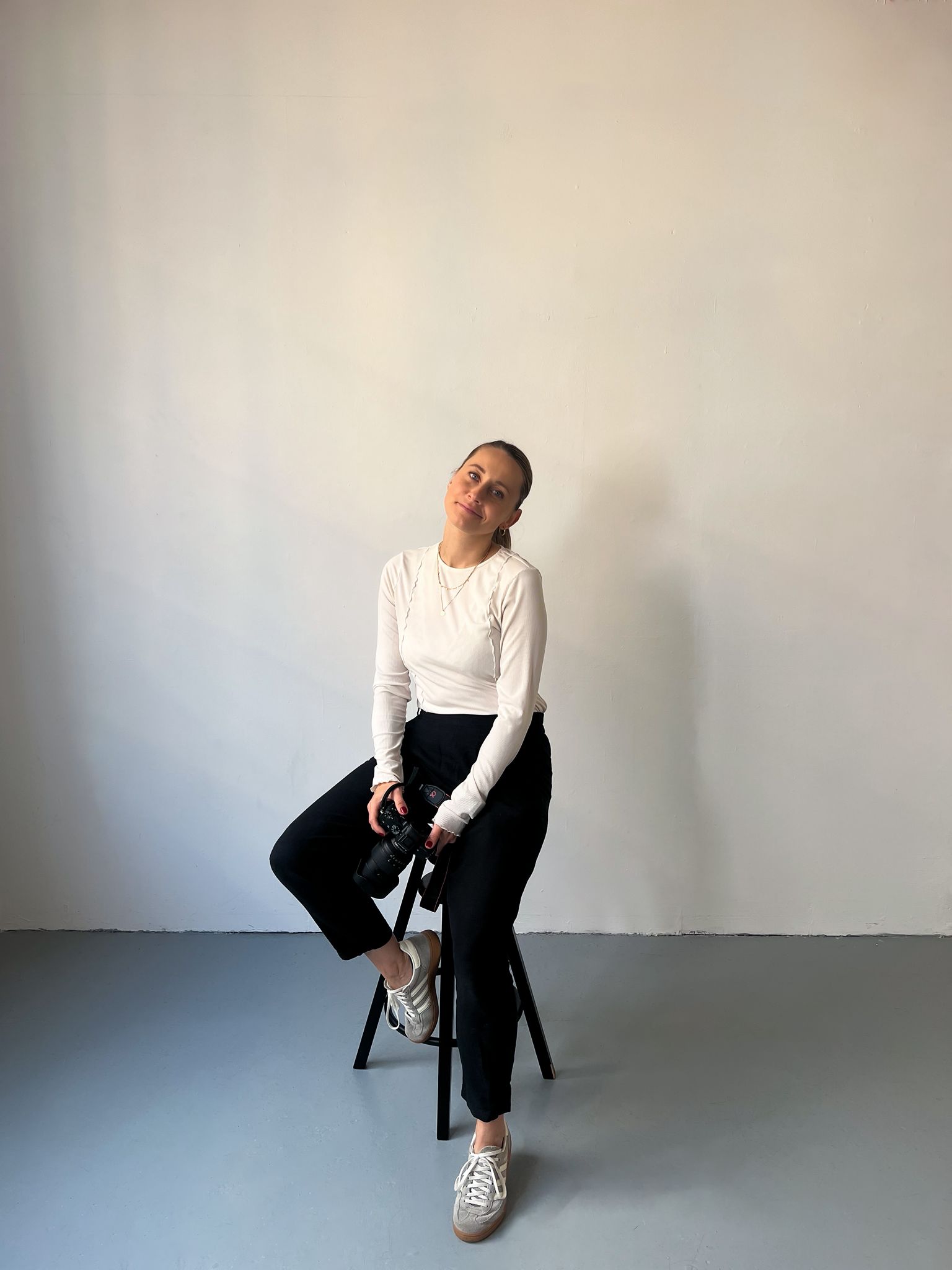 woman sitting on the bar chair holding a camera and smiling 