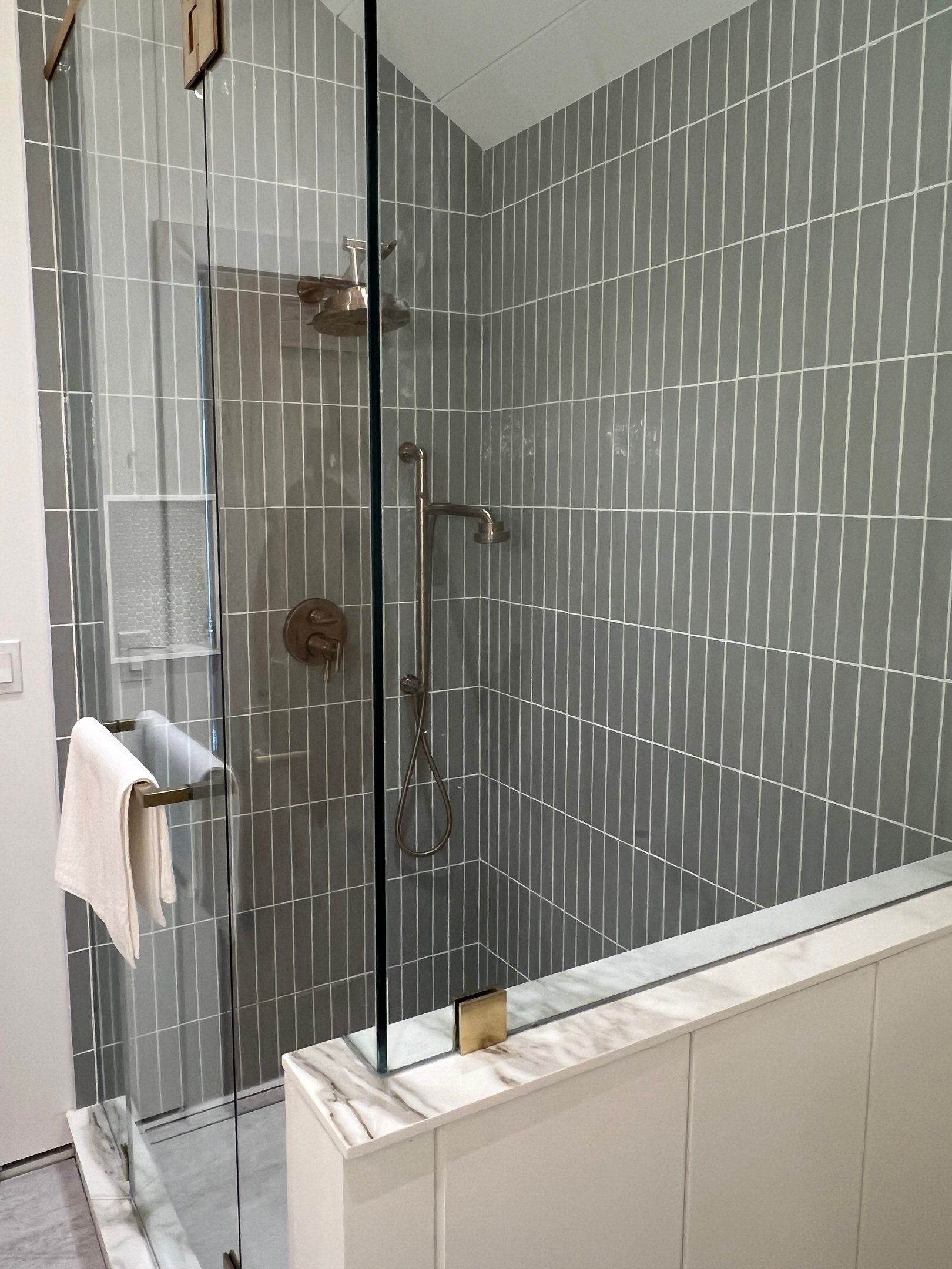 Modern walk-in shower featuring green vertical subway tiles and frameless glass door.