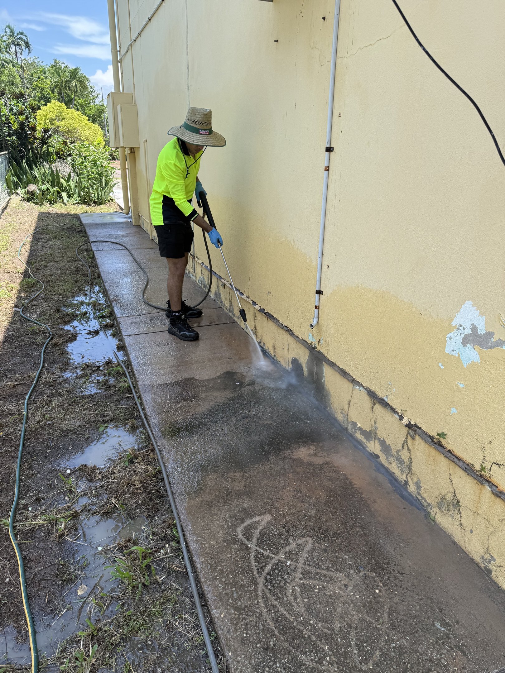 A professional pressure washing technician cleaning a concrete sidewalk and exterior wall.