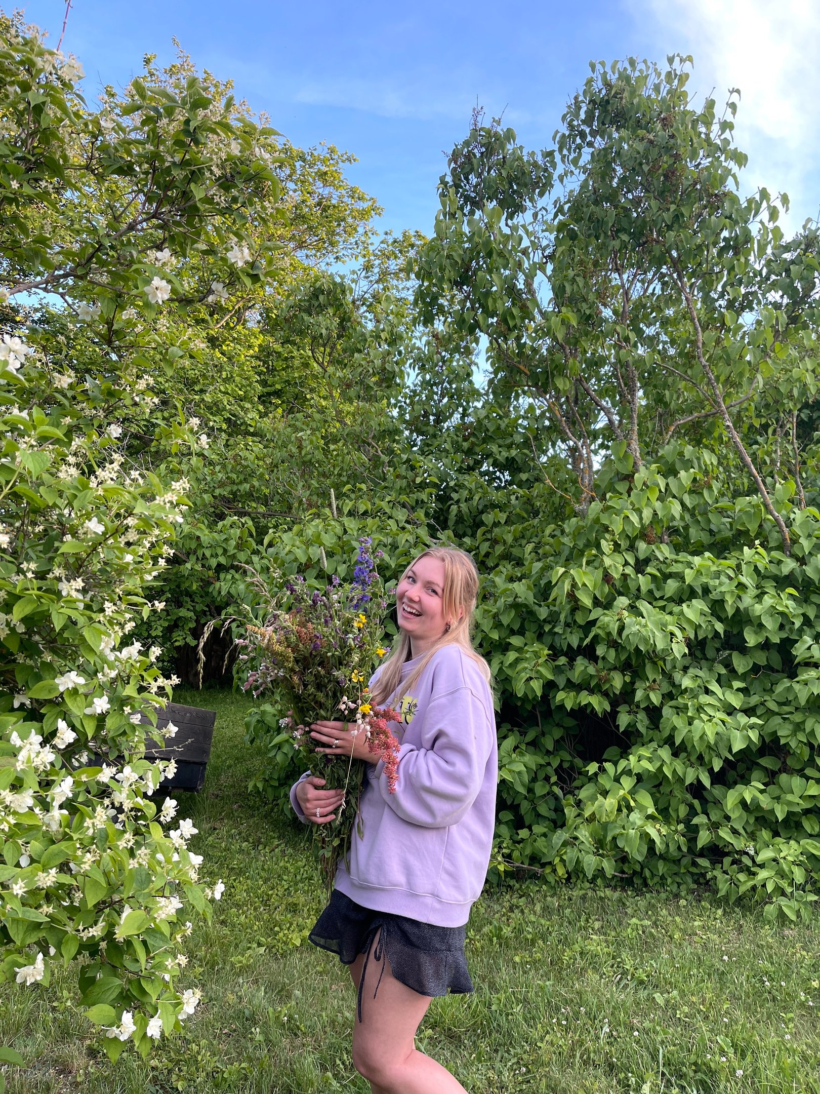 moteris apsirengusi violetiniu megztuku laiko gėles ir juokiasi