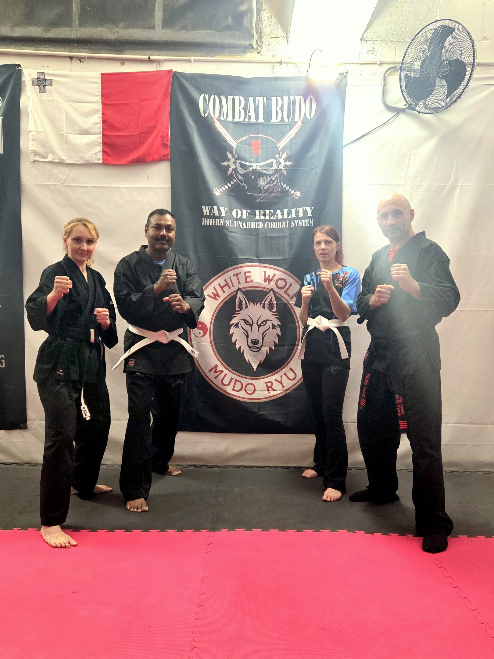 Martial arts practitioners in black gi uniforms posing in a Combat Budo Mudo Ryu training gym.