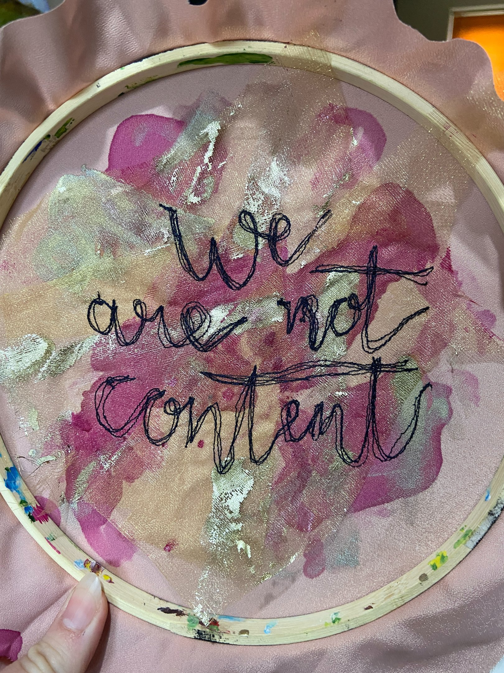 machine embroidered text which says 'we are not content' in cursive writing on a pink background