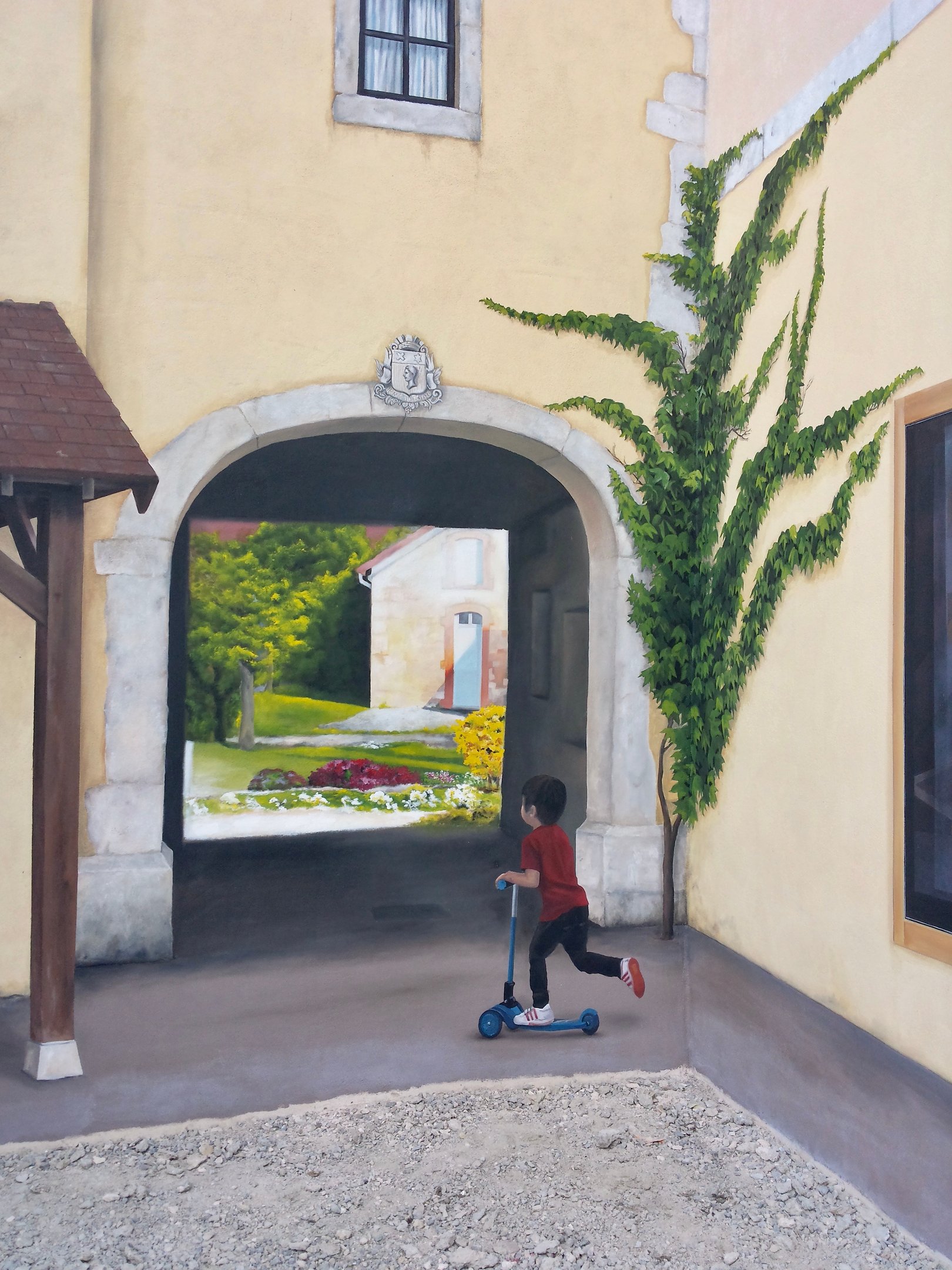 Détail d'une fresque sur façade à Moirans-en-Montagne: un garçon en trottinette devant un porche.