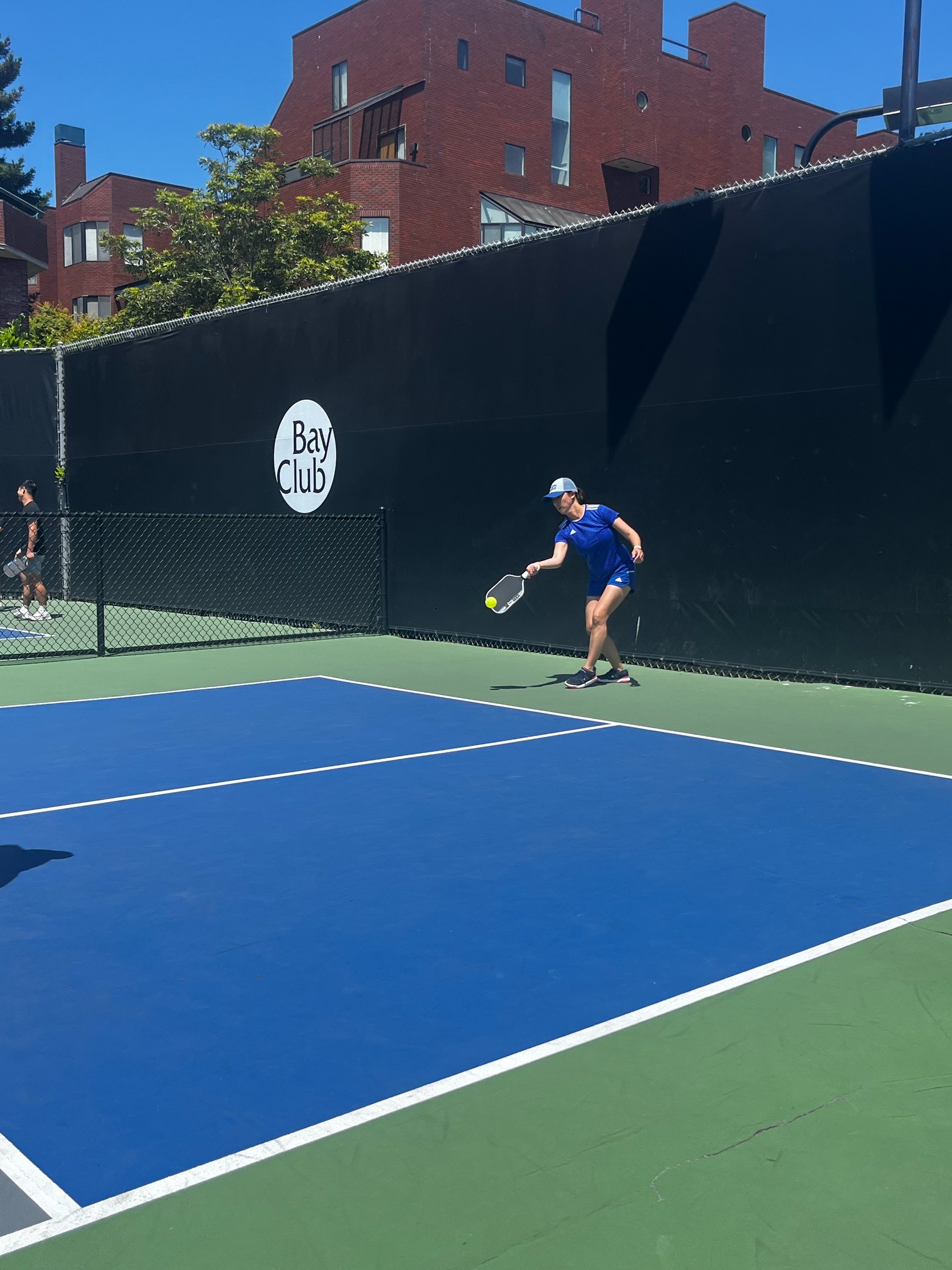 Pickleball player in blue outfit reaching for a low shot during pickleball training match.