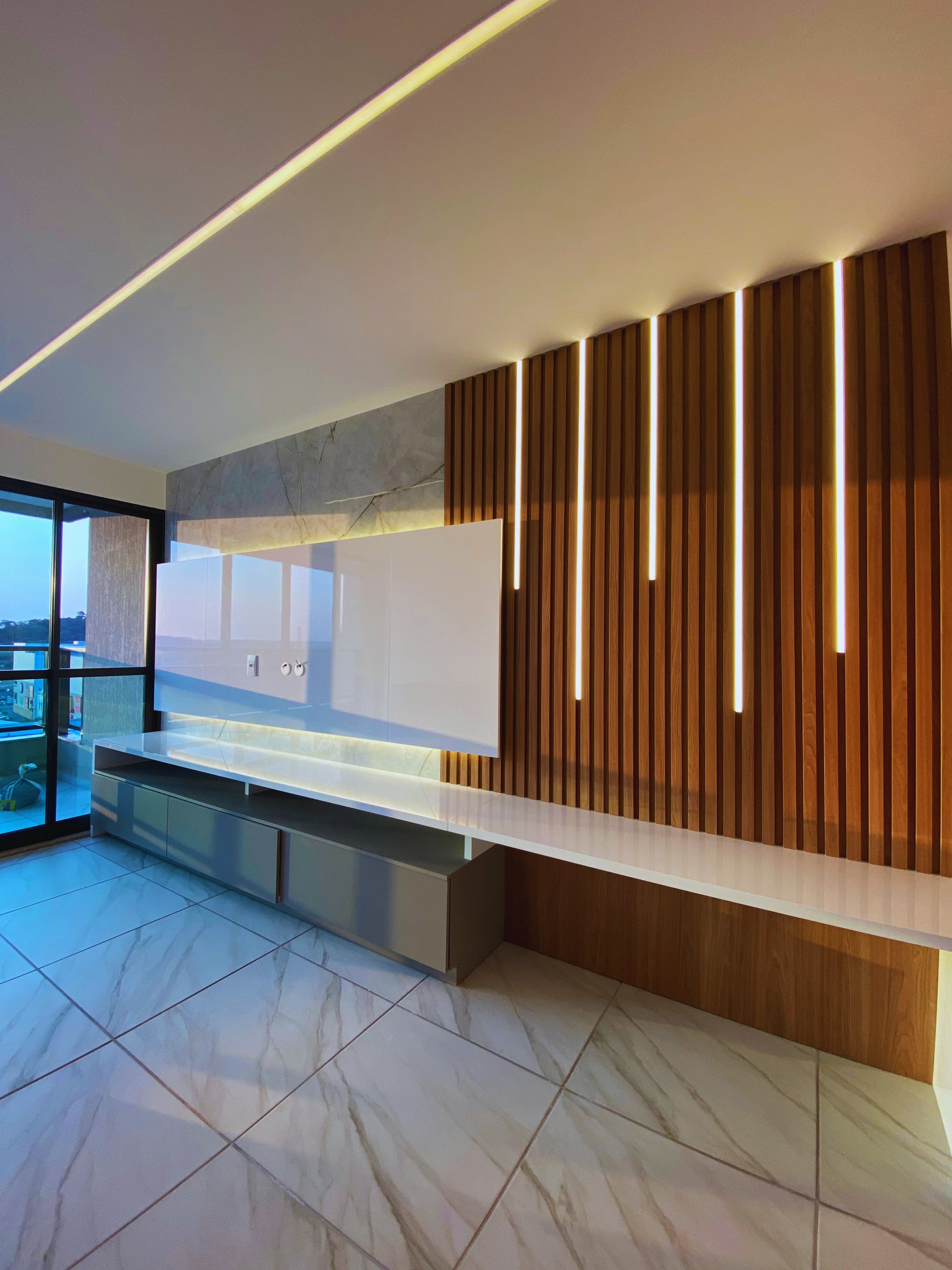 Sala reformada pela Nattú Engenharia com painel de madeira iluminado e piso de porcelanato claro