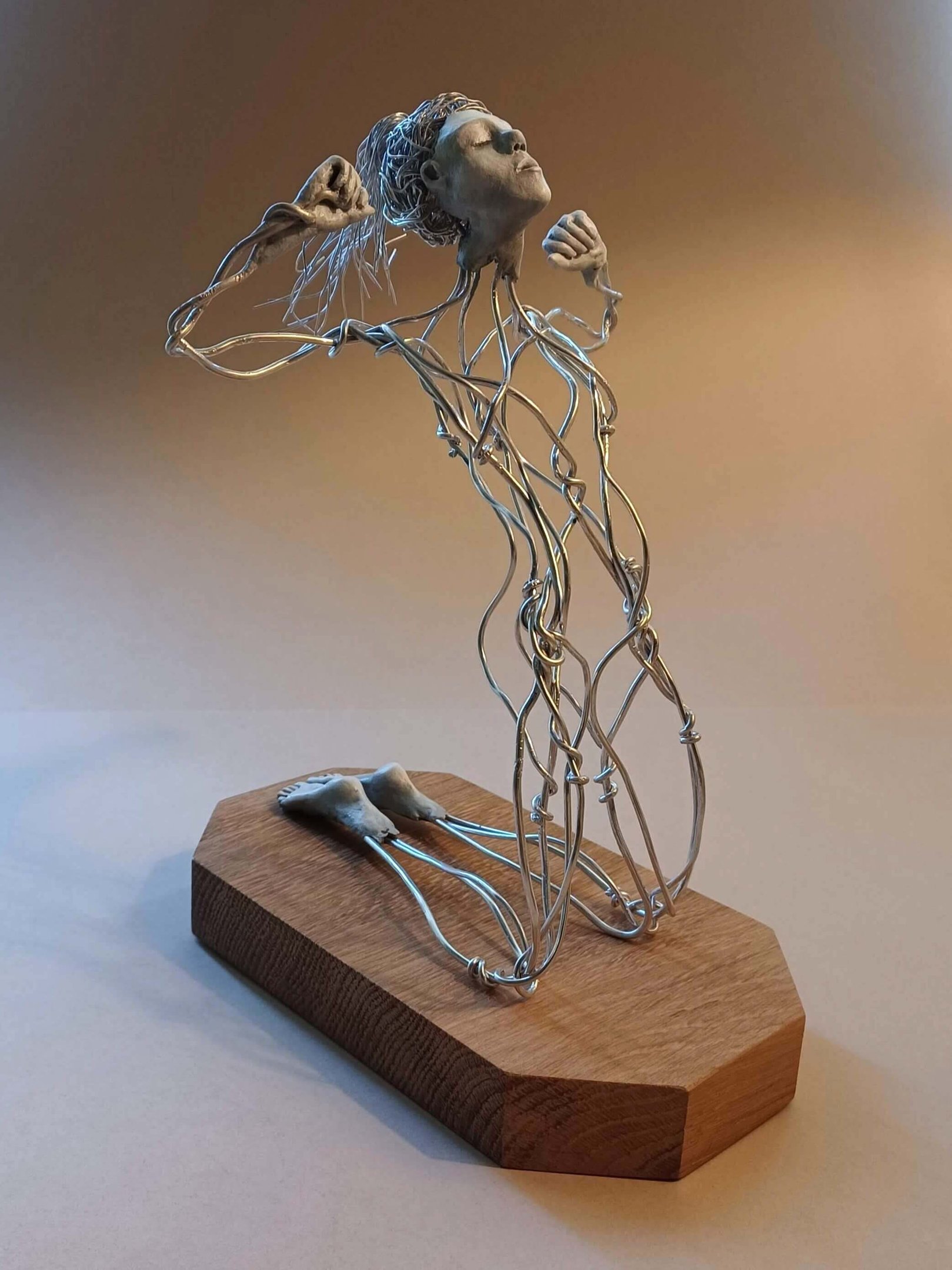 A wire sculpture of a complete kneeling female figure with clay hands, face and feet, arms raised