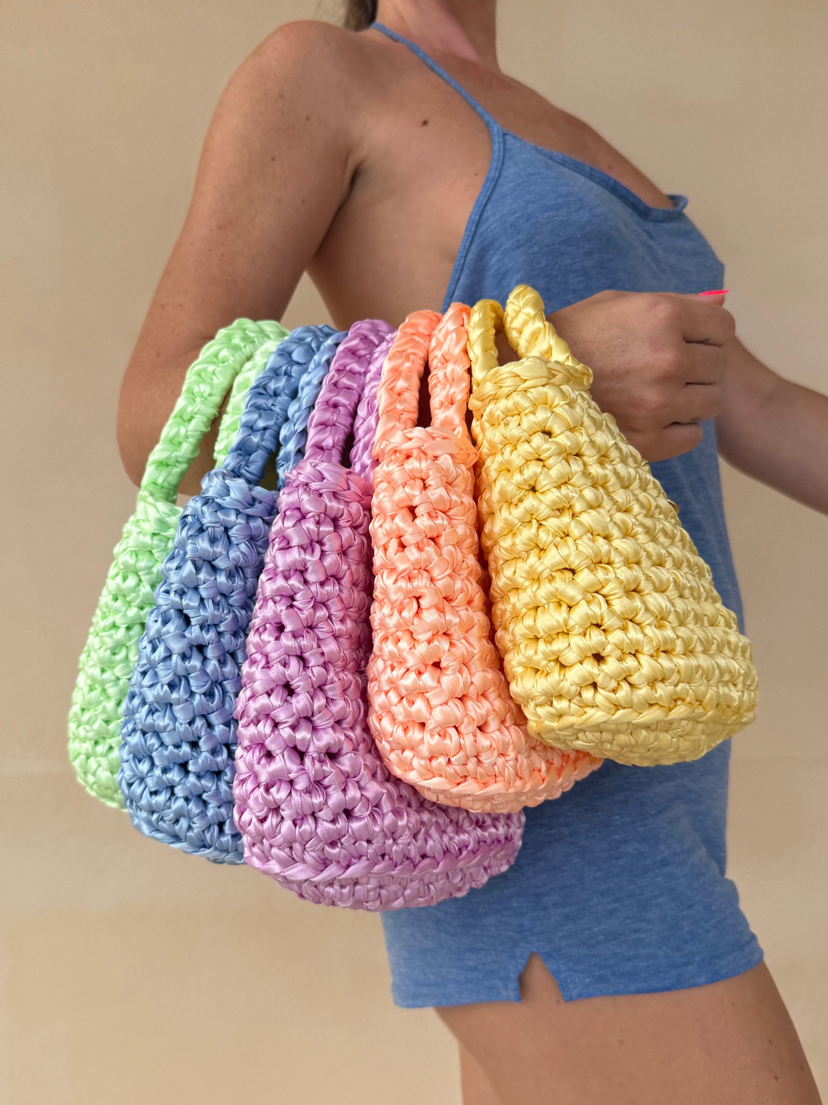 Handmade pastel crochet mini bags in lime, blue, pink, orange, and yellow held by a woman.