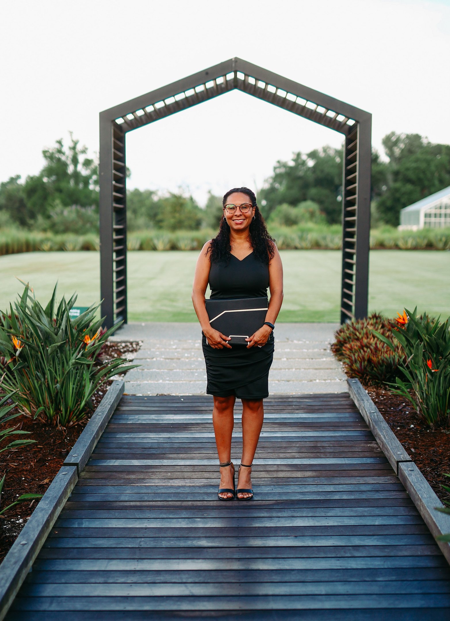 Professional woman in black dress holding folder at outdoor garden event venue.