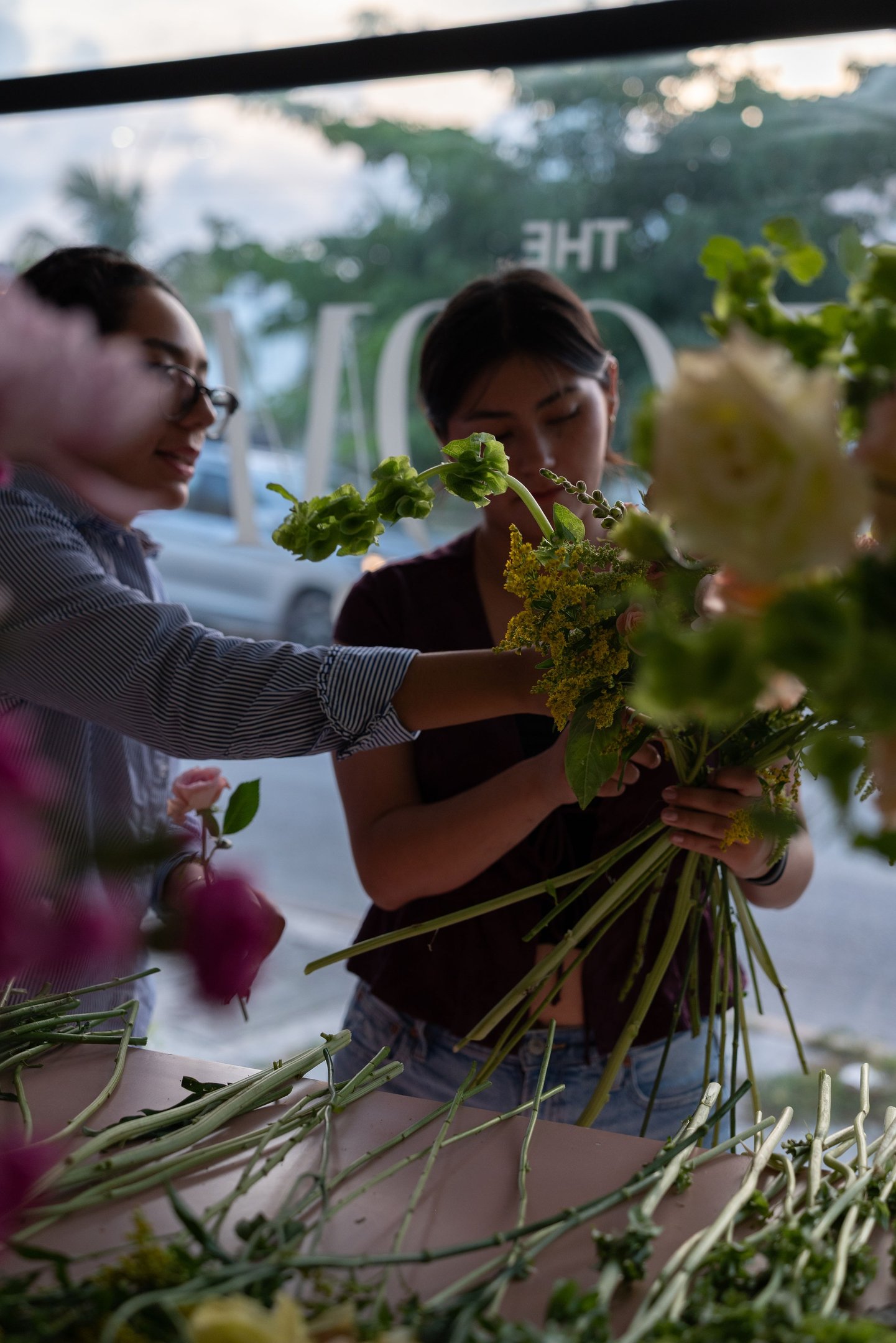 Two professional florists arranging a fresh bouquet of green and yellow flowers in a flower shop.