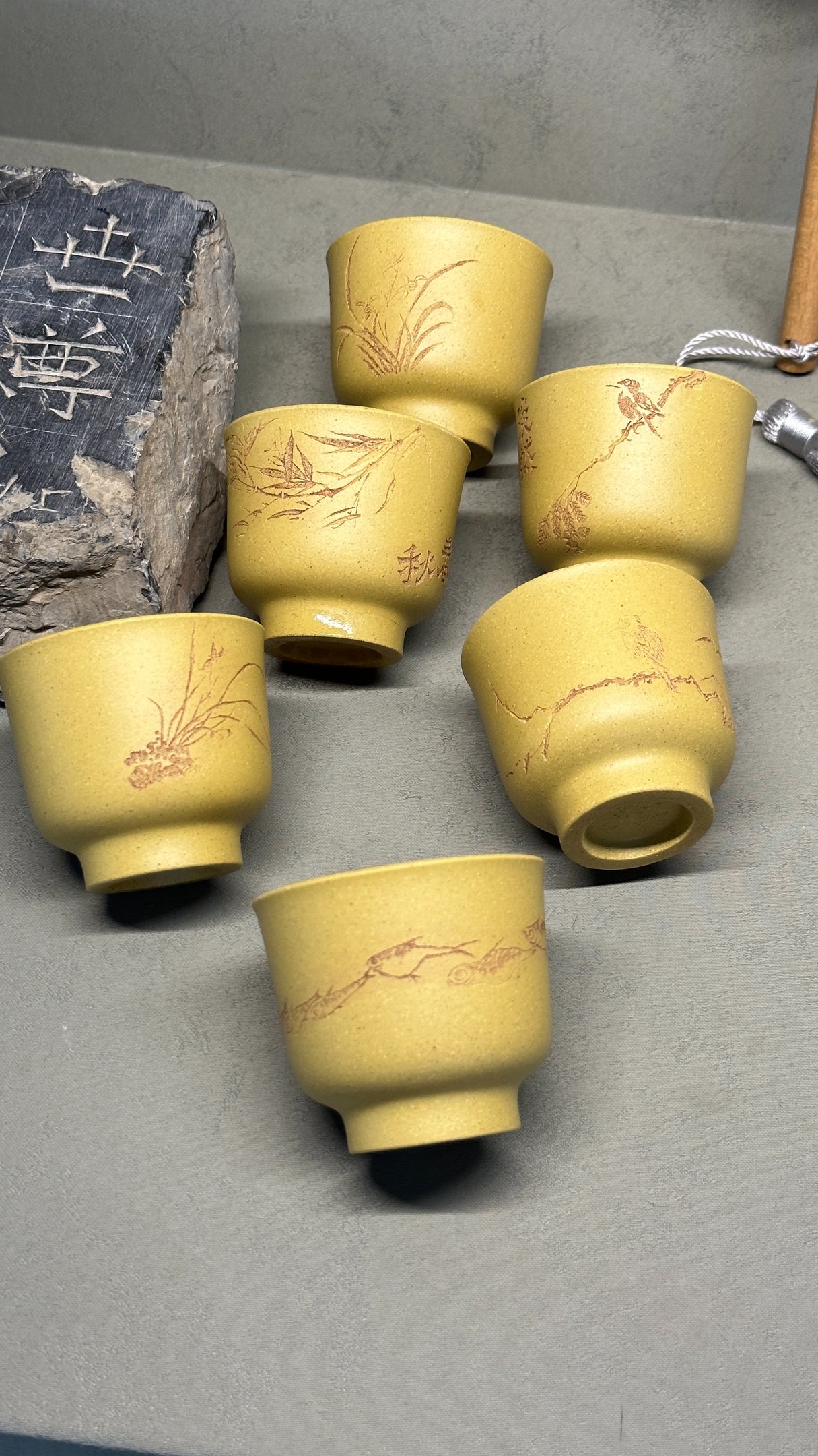 Three yellow teacups engraved with artwork, with an ancient stone beside them