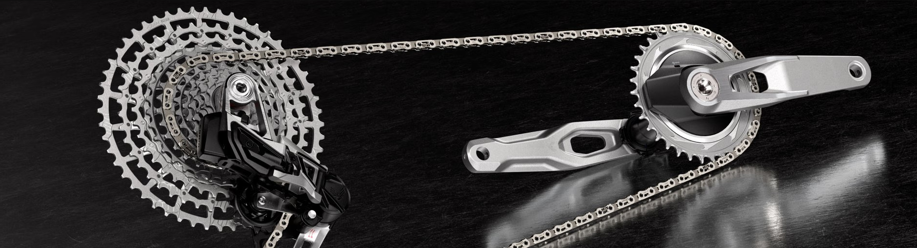 Close-up of a silver bicycle drivetrain featuring a high-performance cassette, chain, and crankset on a dark surface.